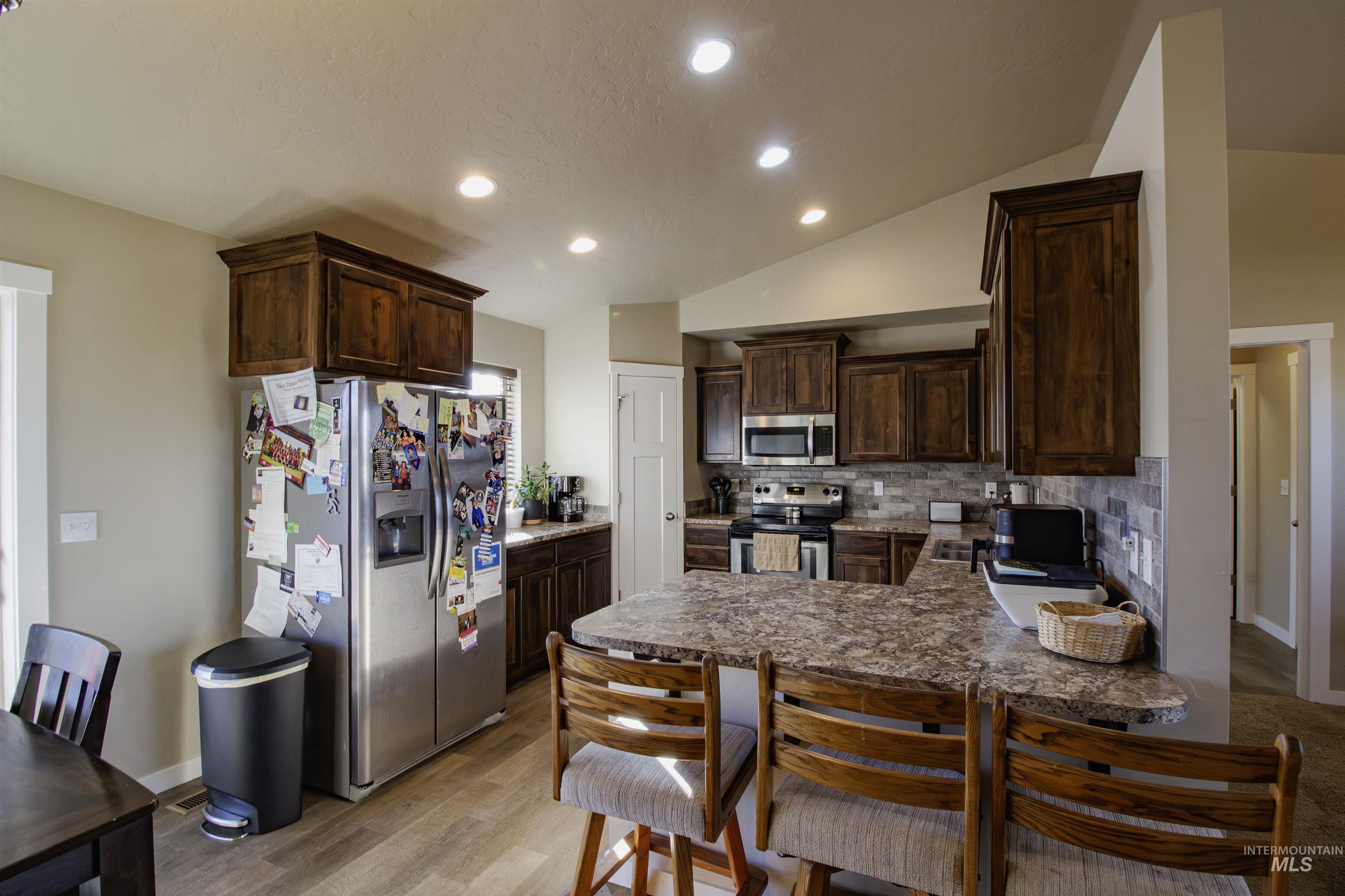 Kitchen featuring dark brown cabinetry, stainless steel appliances, vaulted ceiling, recessed lighting, and a peninsula