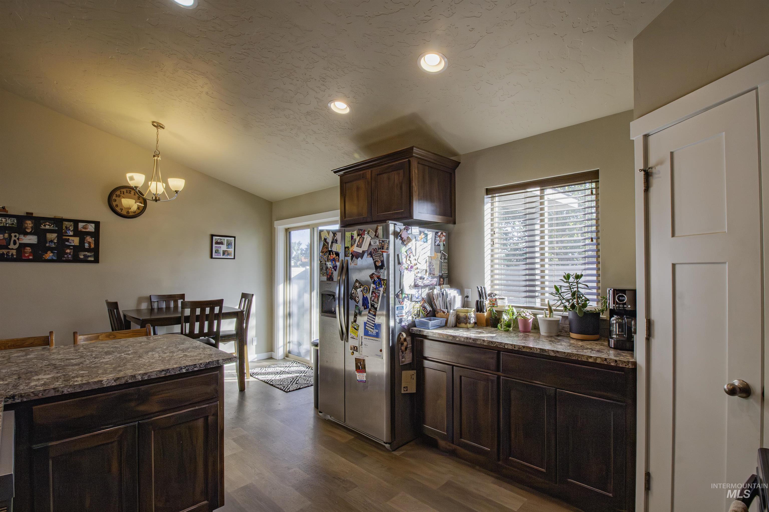 Kitchen featuring dark brown cabinets, a textured ceiling, stainless steel refrigerator with ice dispenser, lofted ceiling, and healthy amount of natural light