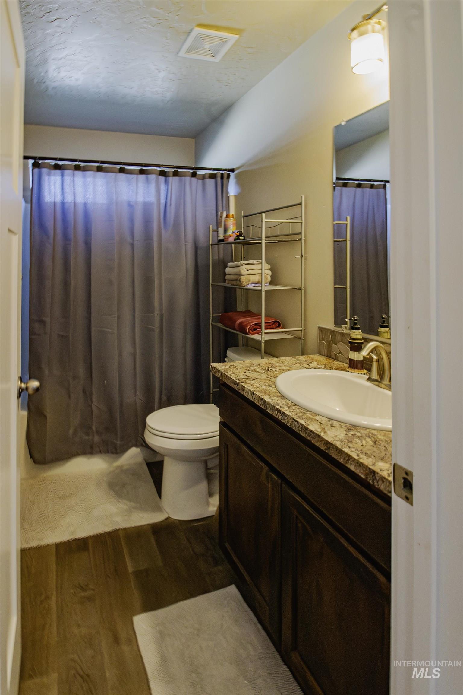 Full bathroom featuring vanity, dark wood-style floors, a textured ceiling, and a shower