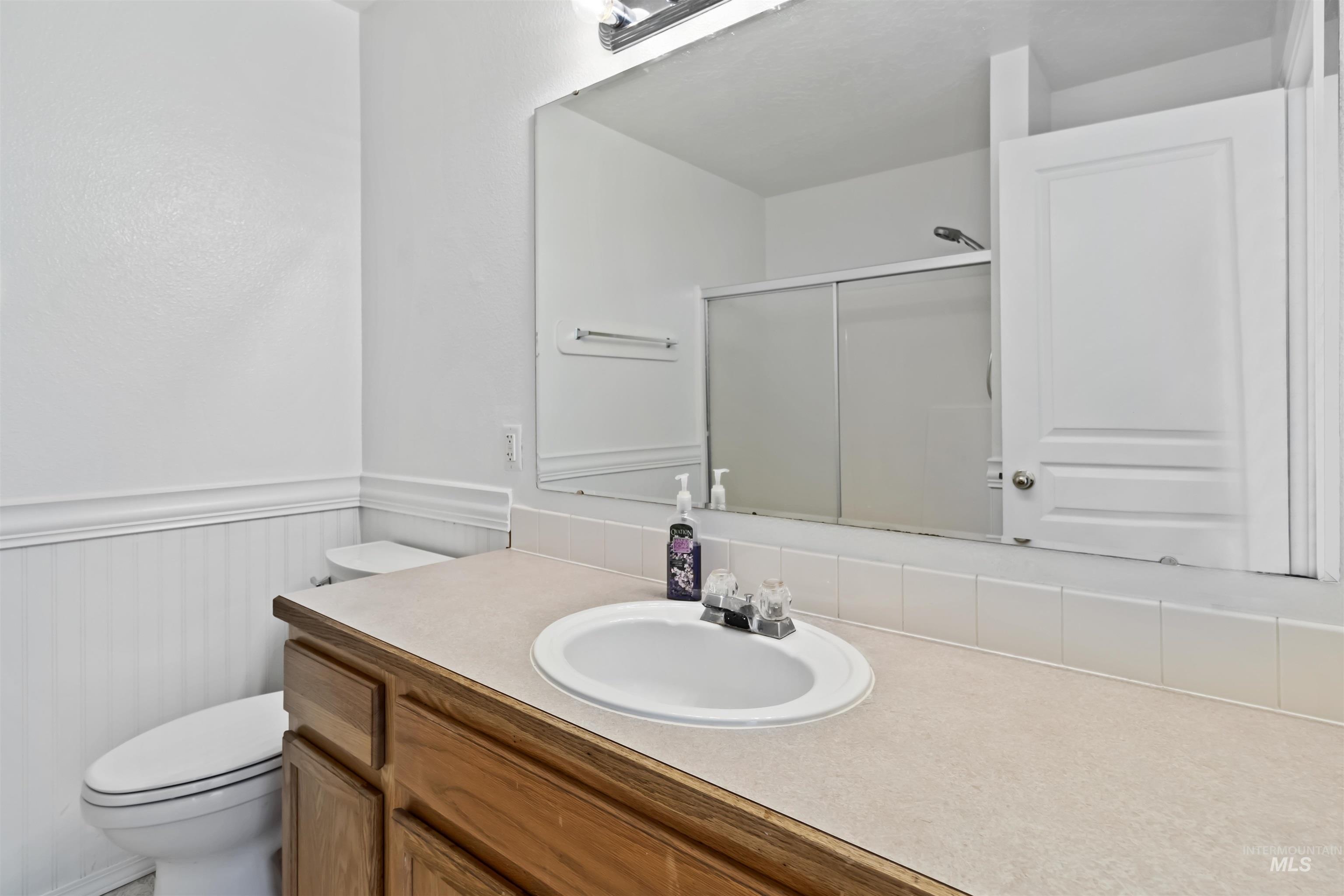 Bathroom with a stall shower, vanity, and a wainscoted wall