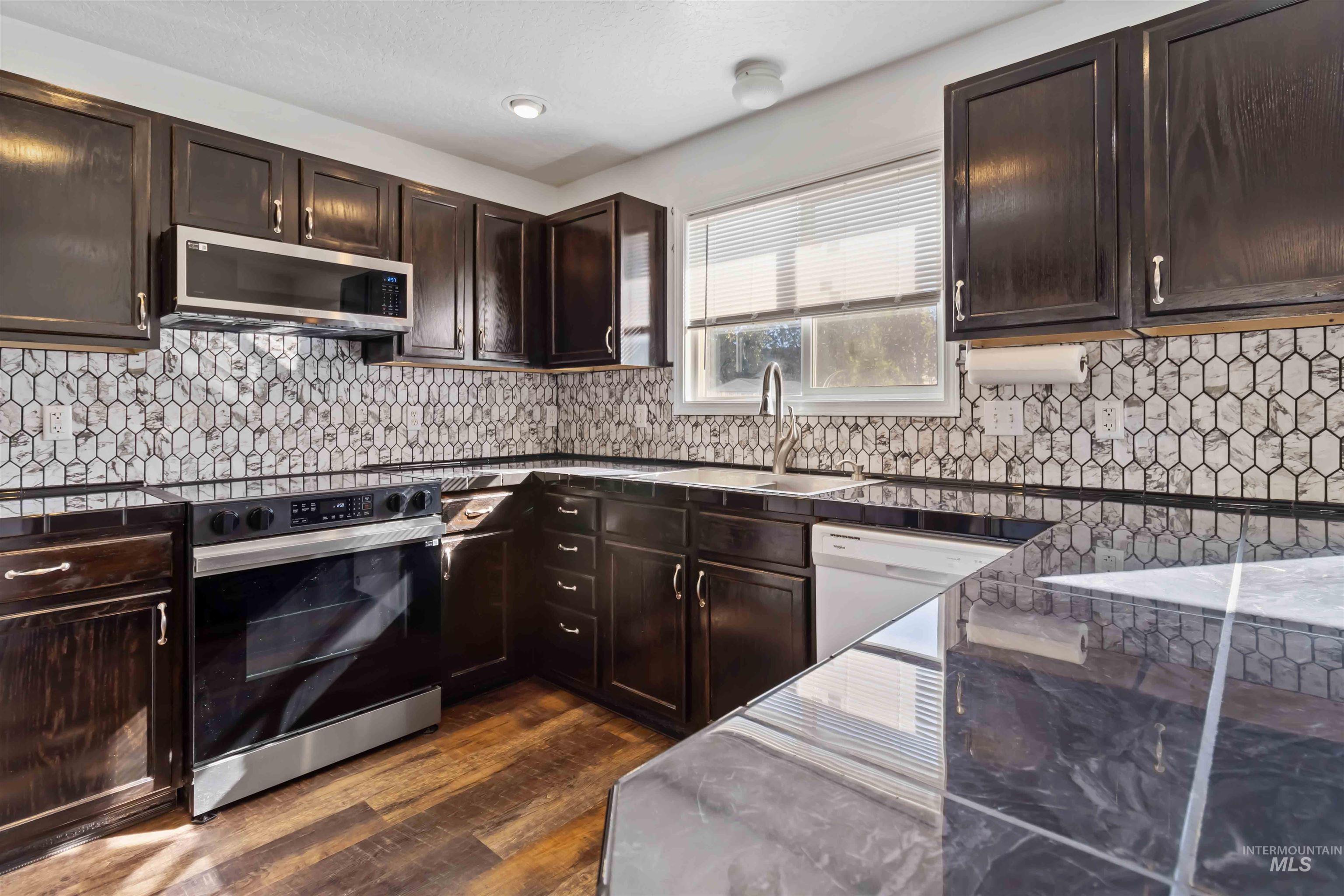 Kitchen featuring dark brown cabinets, electric range oven, dark wood finished floors, stainless steel microwave, and decorative backsplash