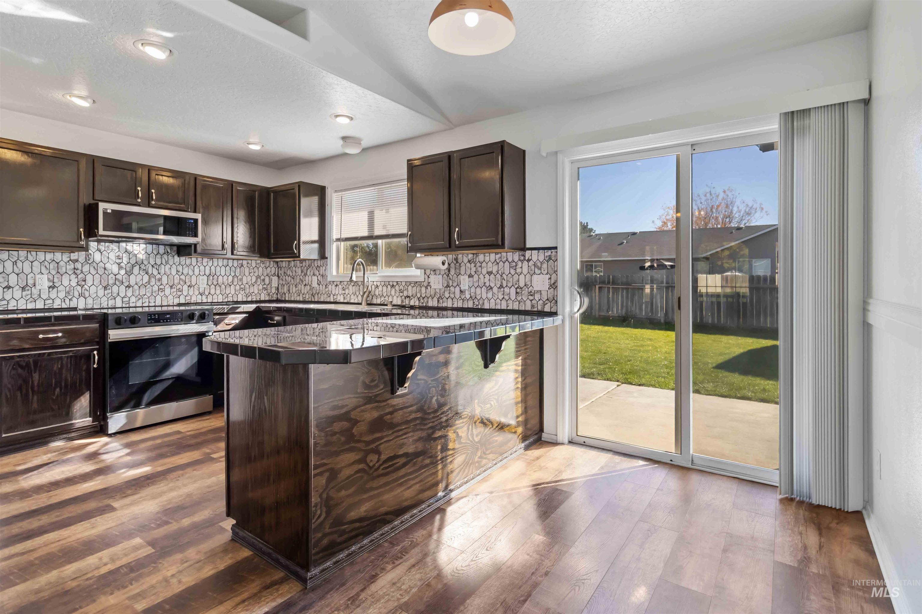 Kitchen with dark brown cabinets, decorative backsplash, dark wood finished floors, appliances with stainless steel finishes, and a textured ceiling