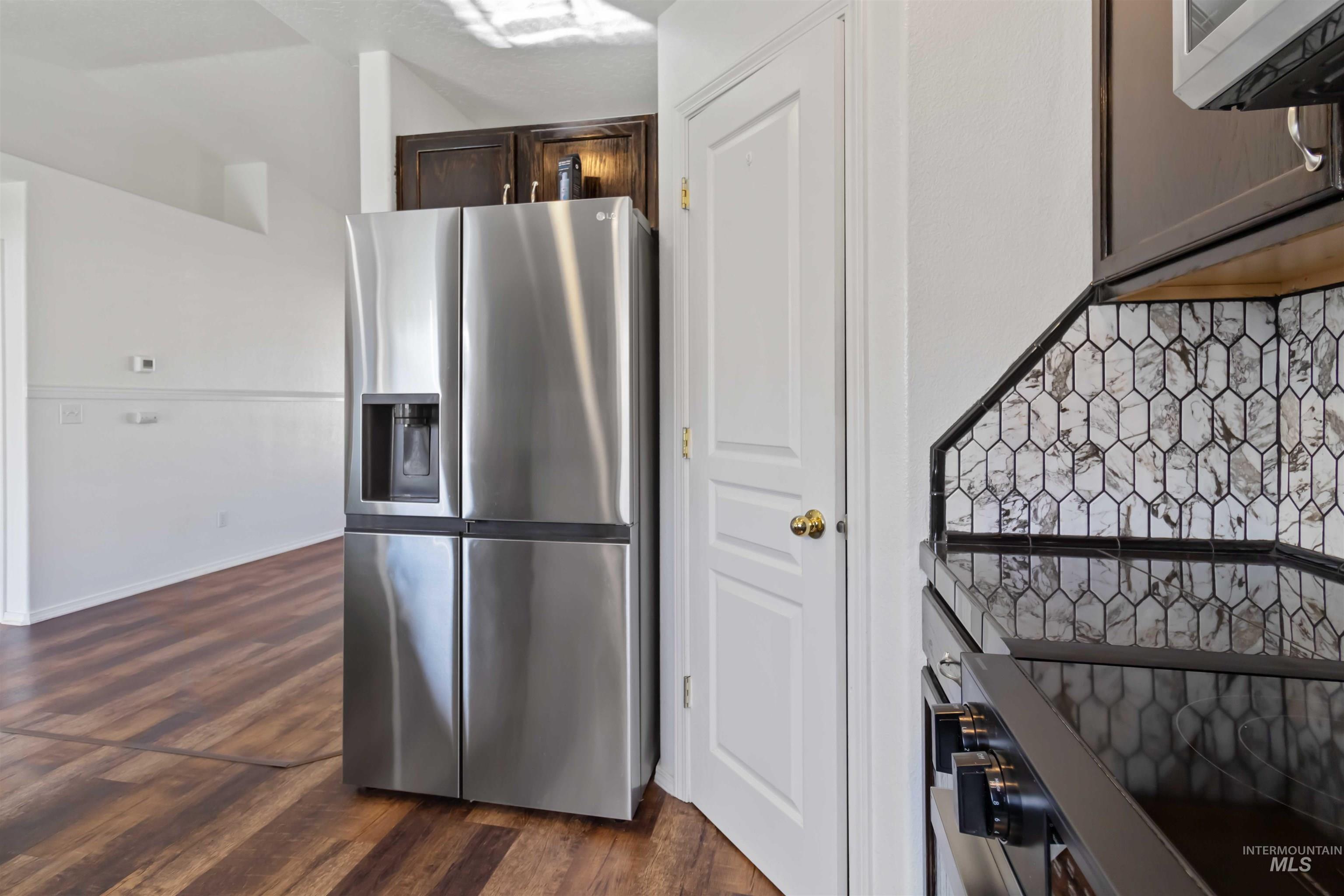 Kitchen with stainless steel refrigerator with ice dispenser, dark wood-style floors, black electric range oven, and dark brown cabinetry