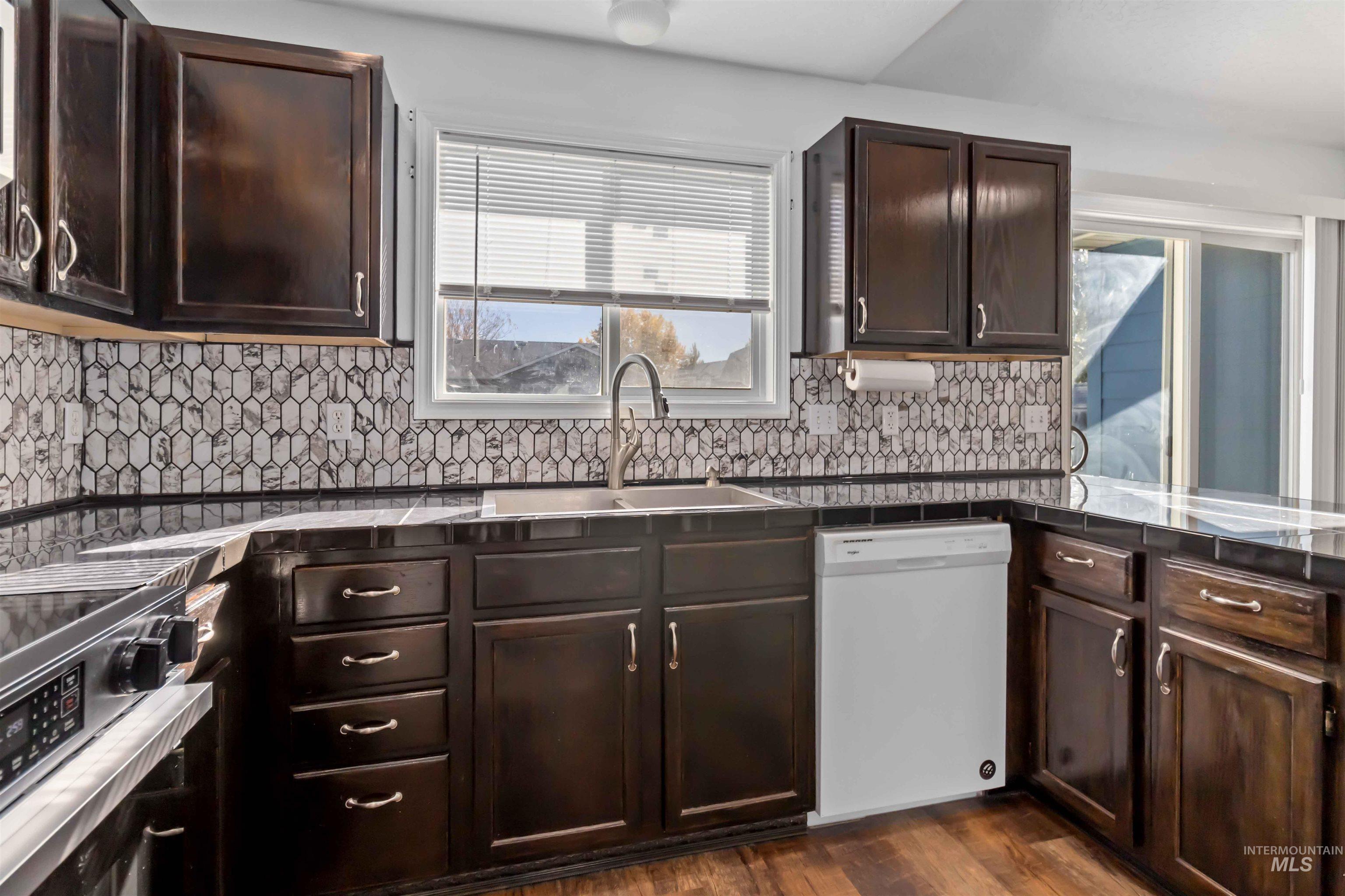 Kitchen with dark brown cabinets, dishwasher, dark countertops, and dark wood finished floors