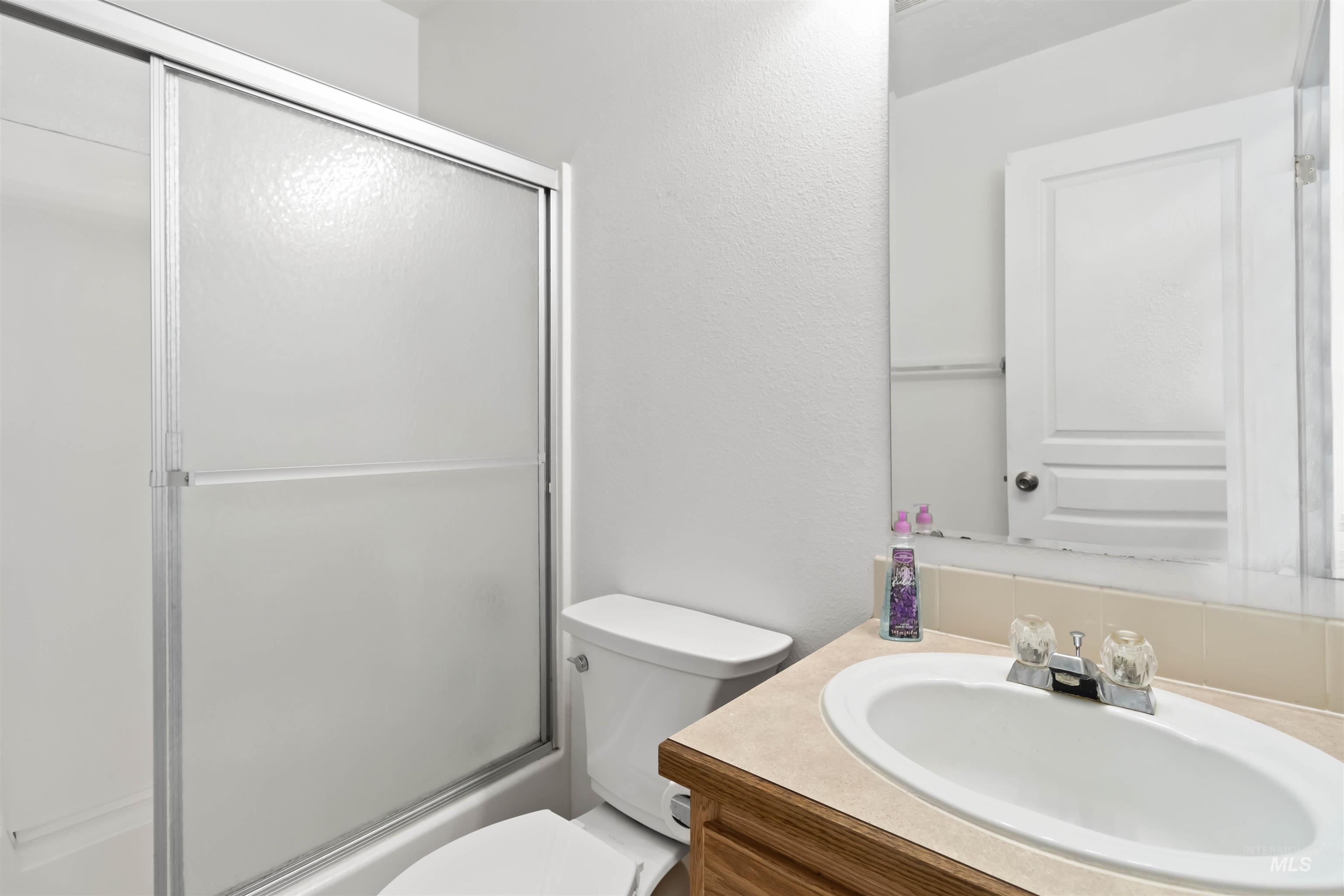 Bathroom with vanity, enclosed tub / shower combo, and a textured wall