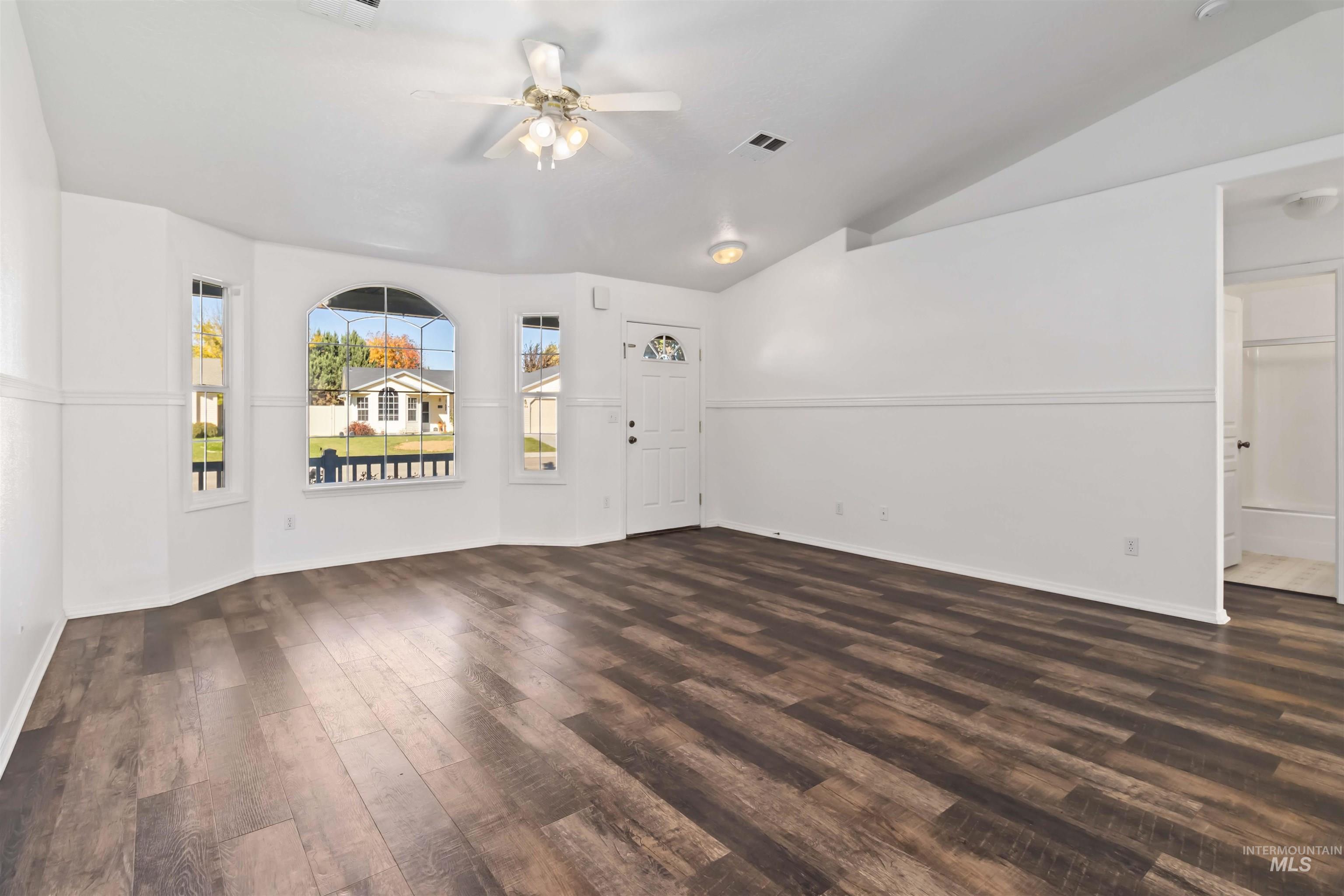 Unfurnished living room with dark wood finished floors, vaulted ceiling, and a ceiling fan