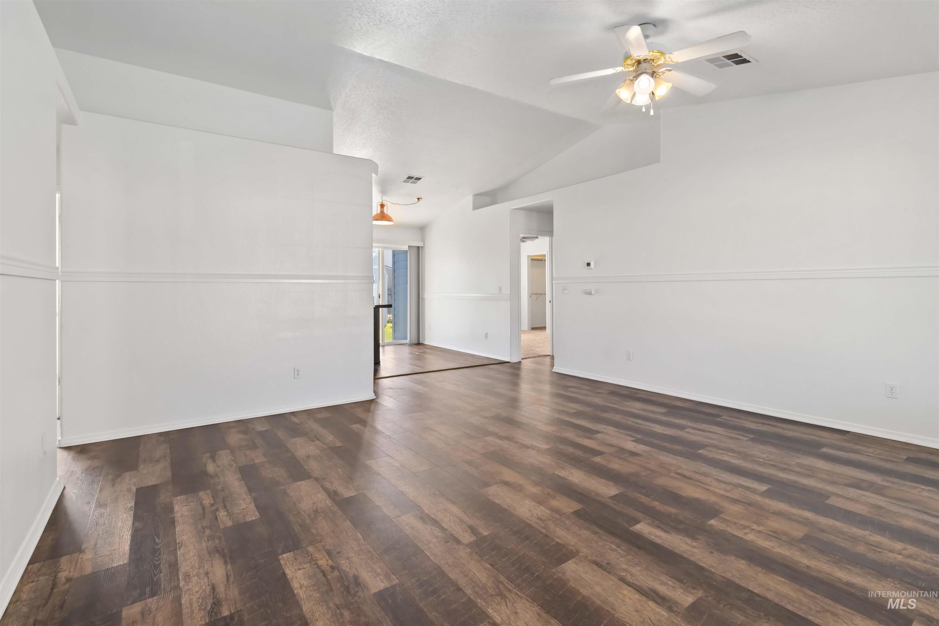 Empty room with dark wood-style flooring, vaulted ceiling, and a ceiling fan