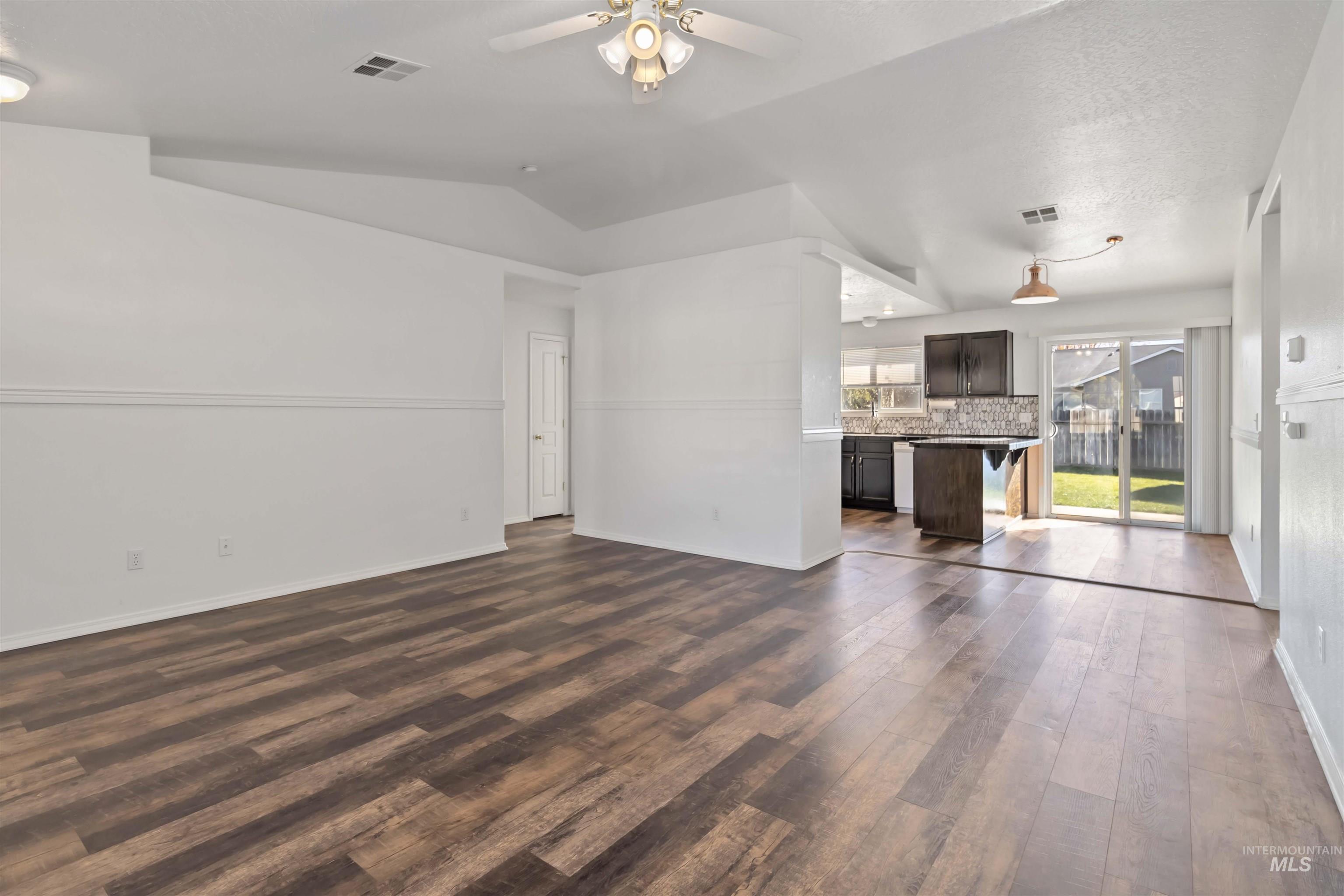 Unfurnished living room featuring dark wood-style flooring, ceiling fan, lofted ceiling, and a textured ceiling