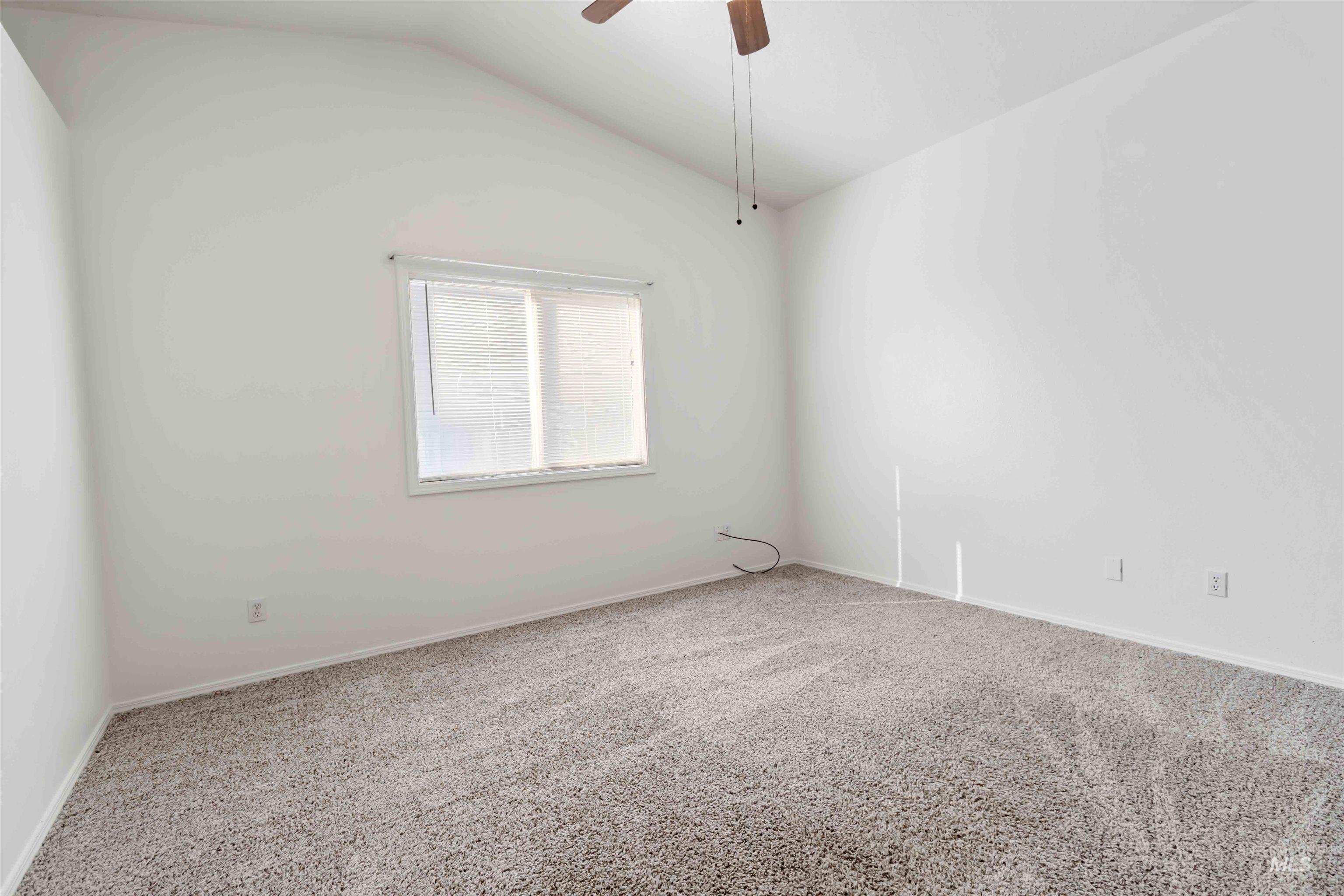 Carpeted spare room featuring vaulted ceiling and ceiling fan