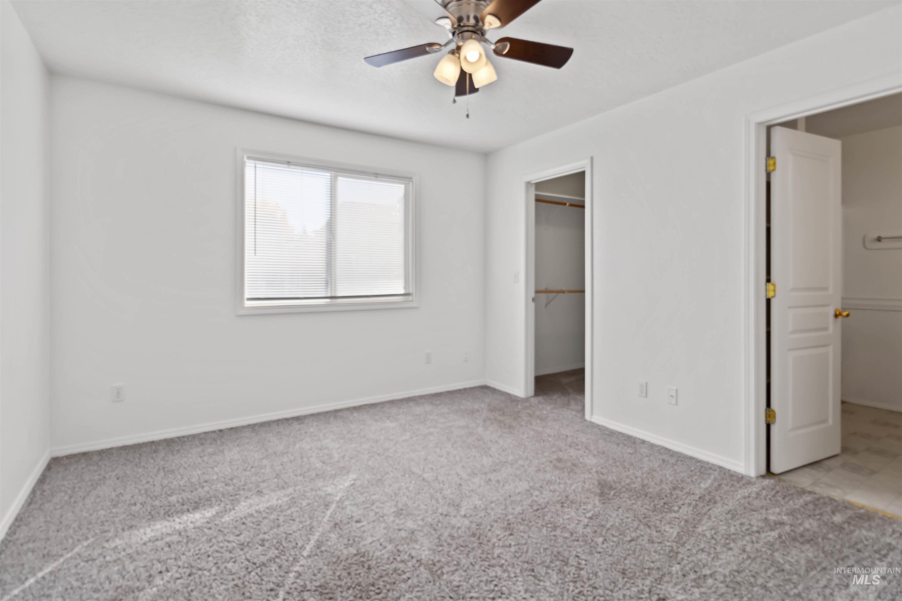 Unfurnished bedroom with a spacious closet, light colored carpet, and a ceiling fan