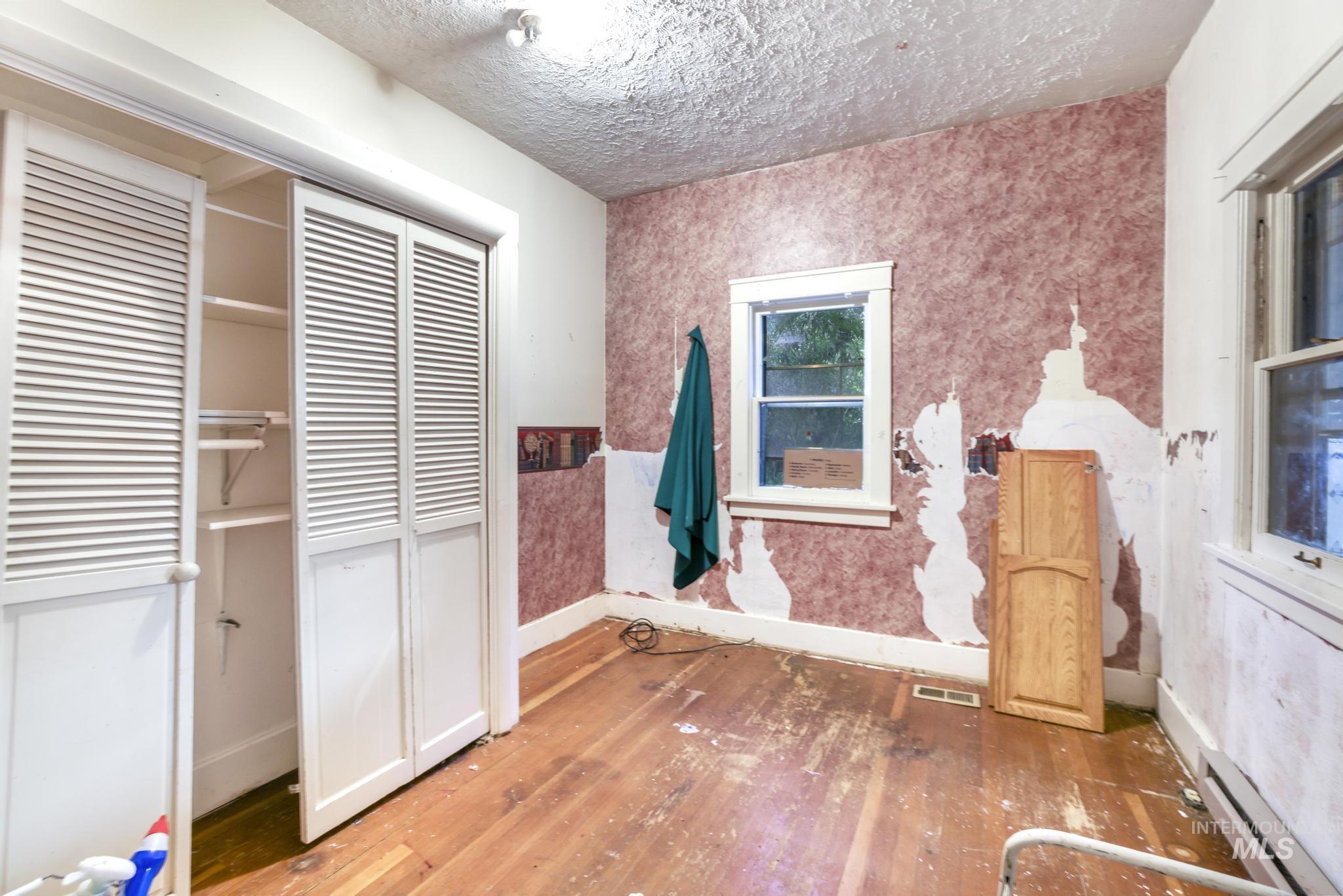 Unfurnished bedroom with wallpapered walls, hardwood / wood-style floors, a baseboard radiator, a closet, and a textured ceiling