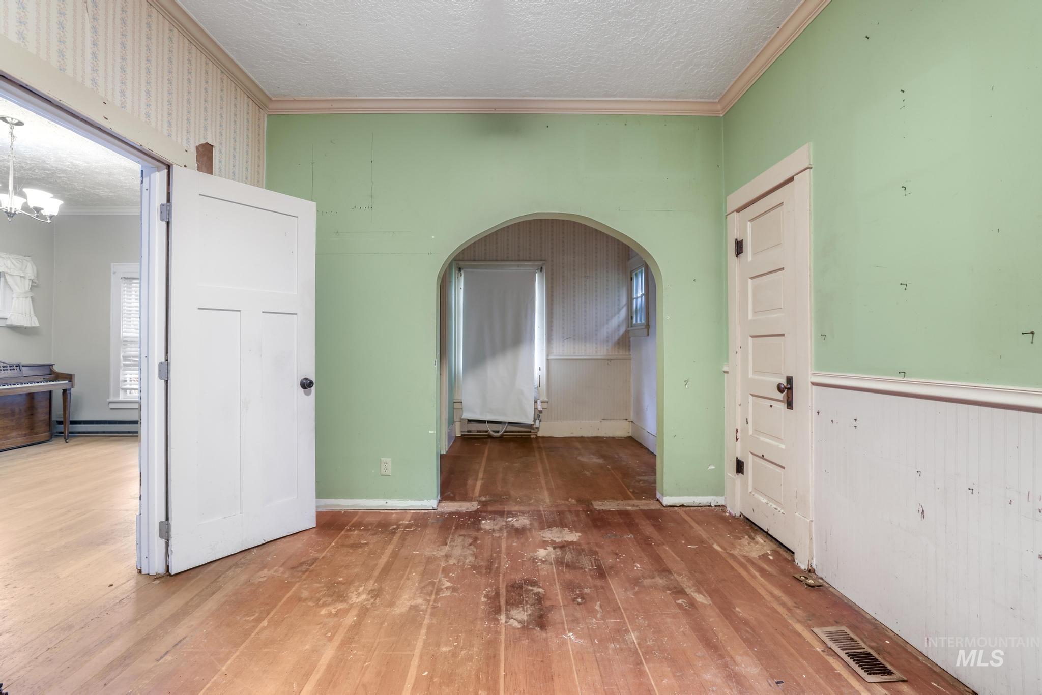 Hallway featuring crown molding, arched walkways, a textured ceiling, wood-type flooring, and wallpapered walls