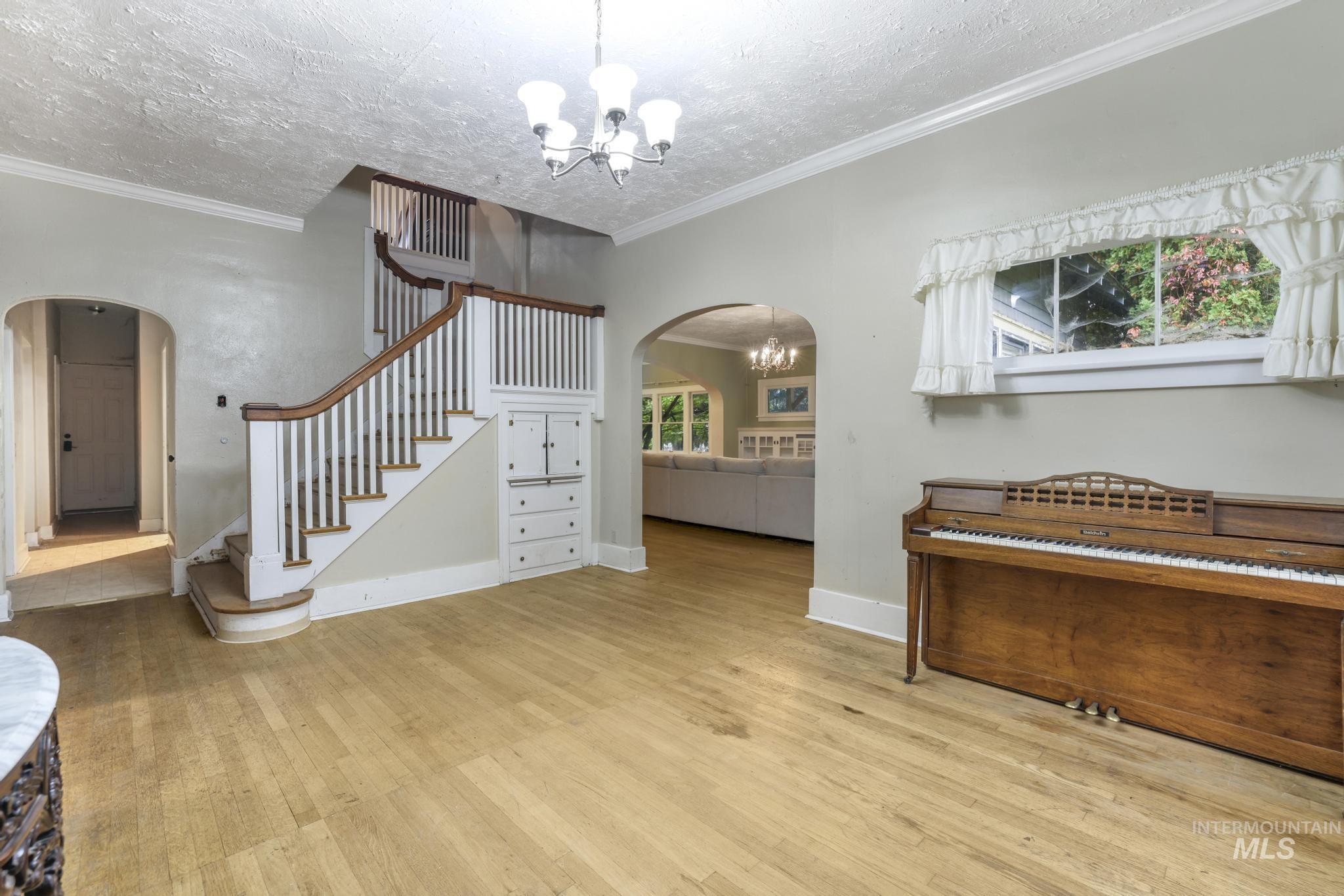 Foyer entrance featuring arched walkways, ornamental molding, stairway, a chandelier, and wood finished floors