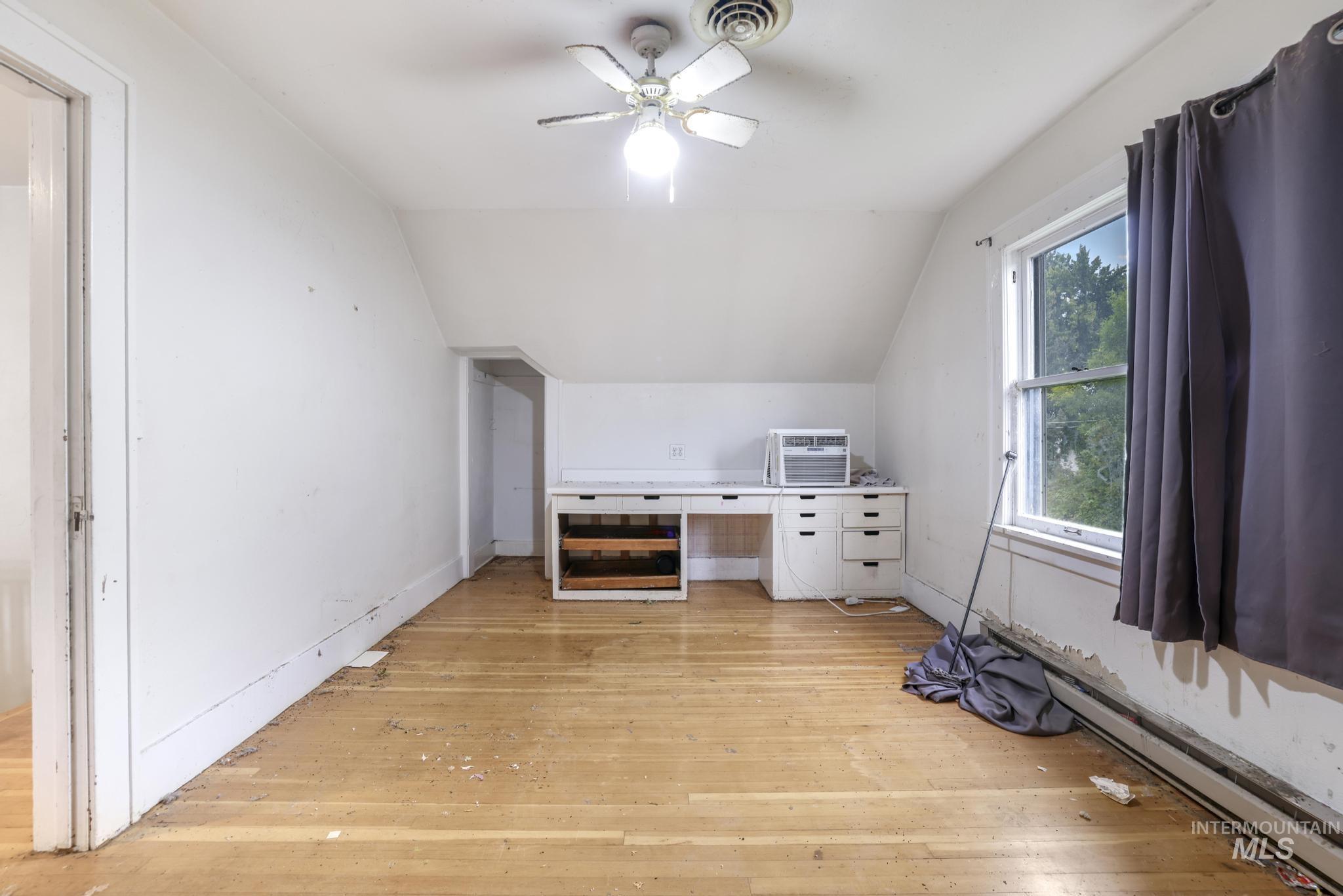 Unfurnished bedroom featuring lofted ceiling, light wood finished floors, a baseboard heating unit, a ceiling fan, and a wall mounted air conditioner