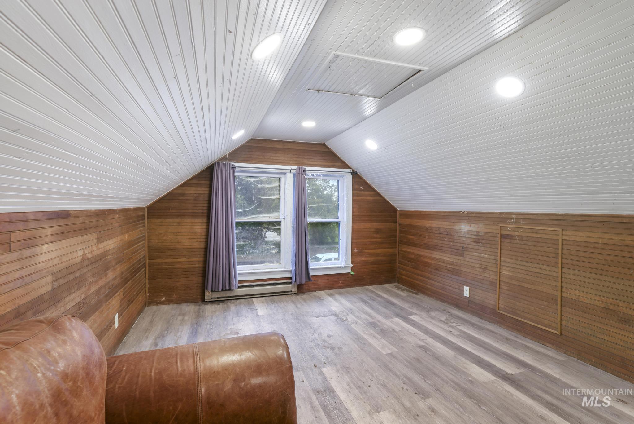 Bedroom with wooden walls, light wood finished floors, vaulted ceiling, and a baseboard heating unit