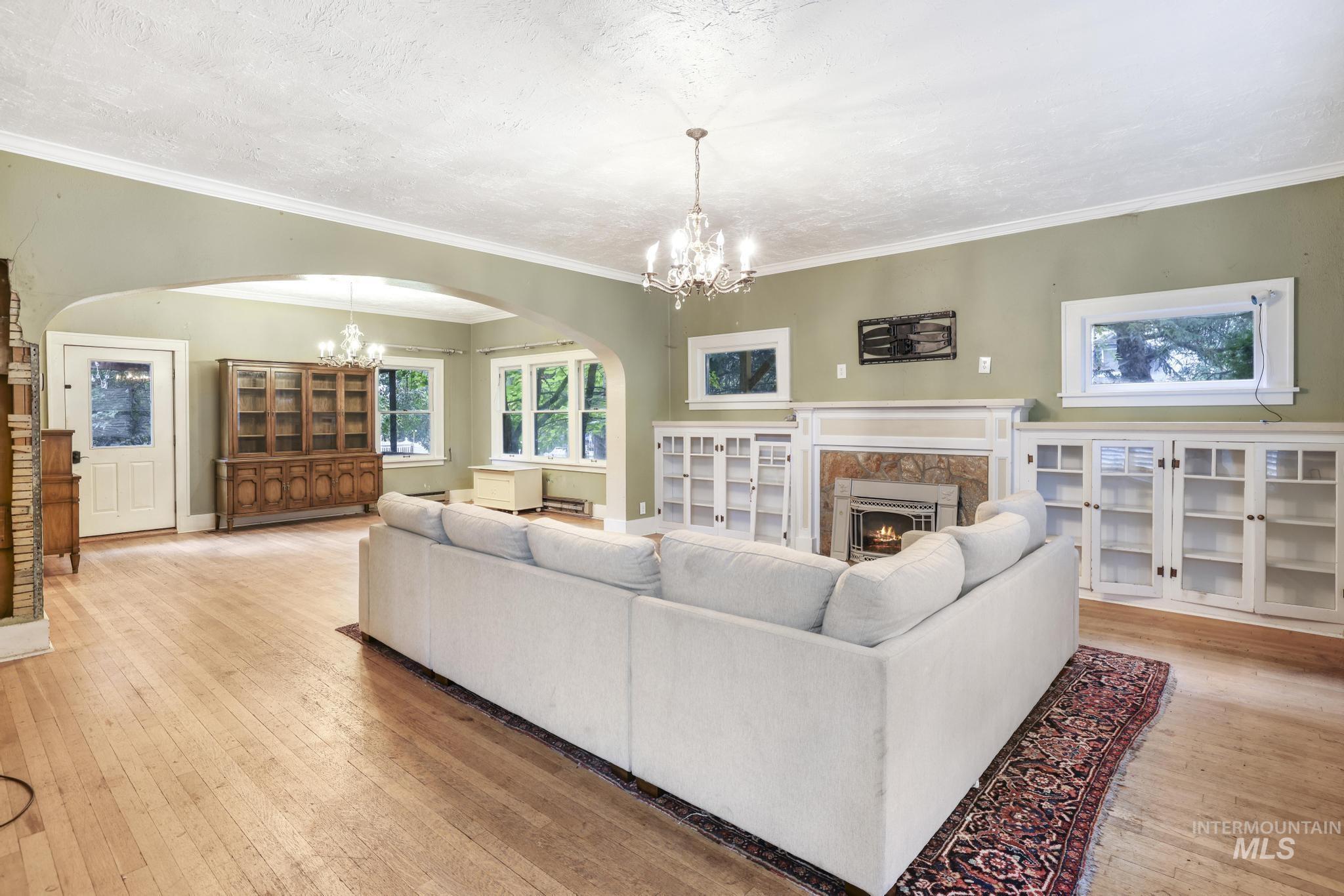Living area with a chandelier, a fireplace, arched walkways, light wood-type flooring, and ornamental molding