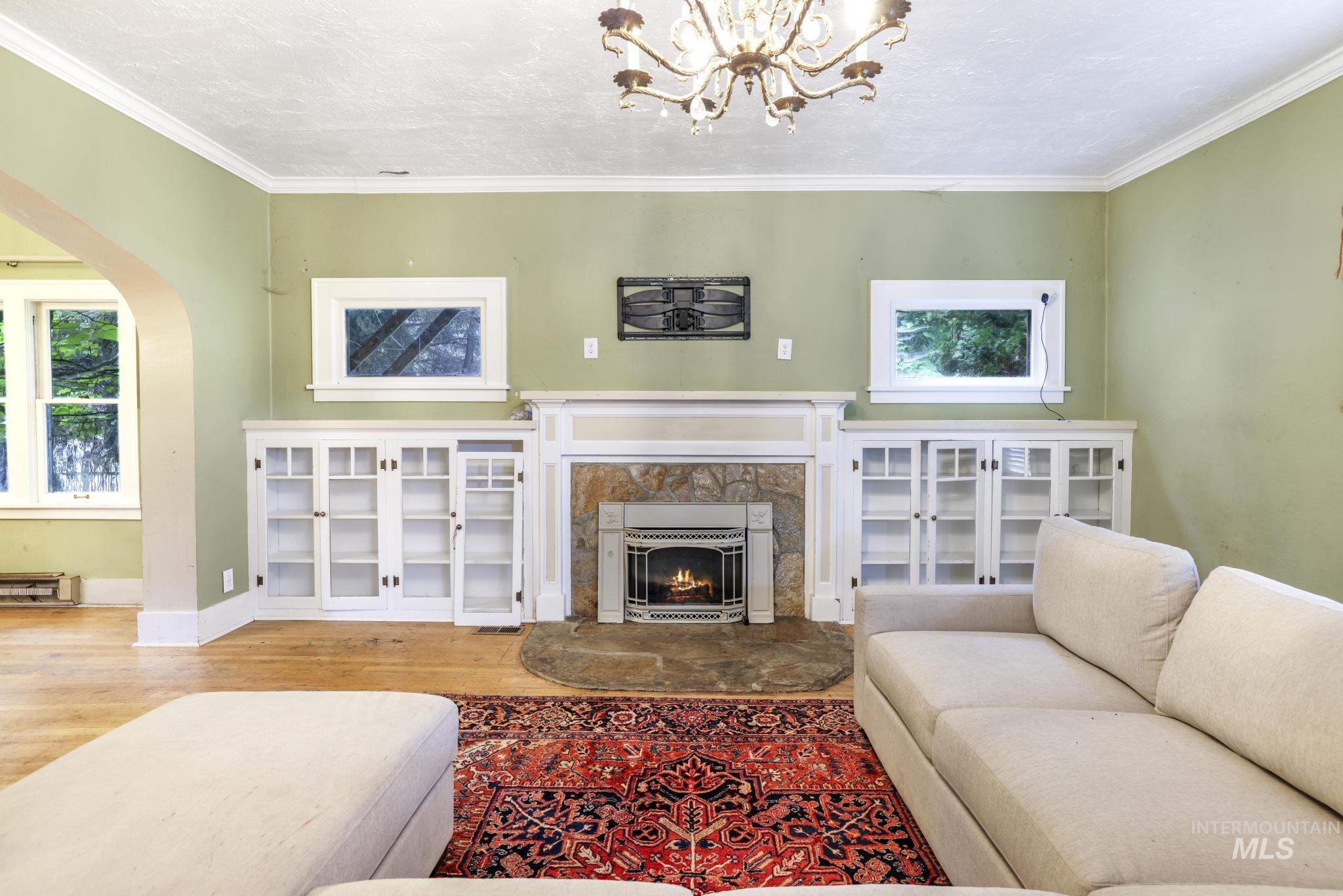 Living area with arched walkways, wood finished floors, crown molding, a fireplace, and a textured ceiling