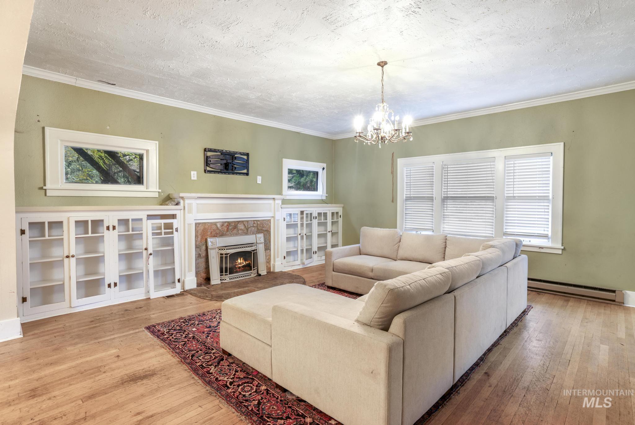 Living area with plenty of natural light, a textured ceiling, light wood-type flooring, a baseboard heating unit, and ornamental molding