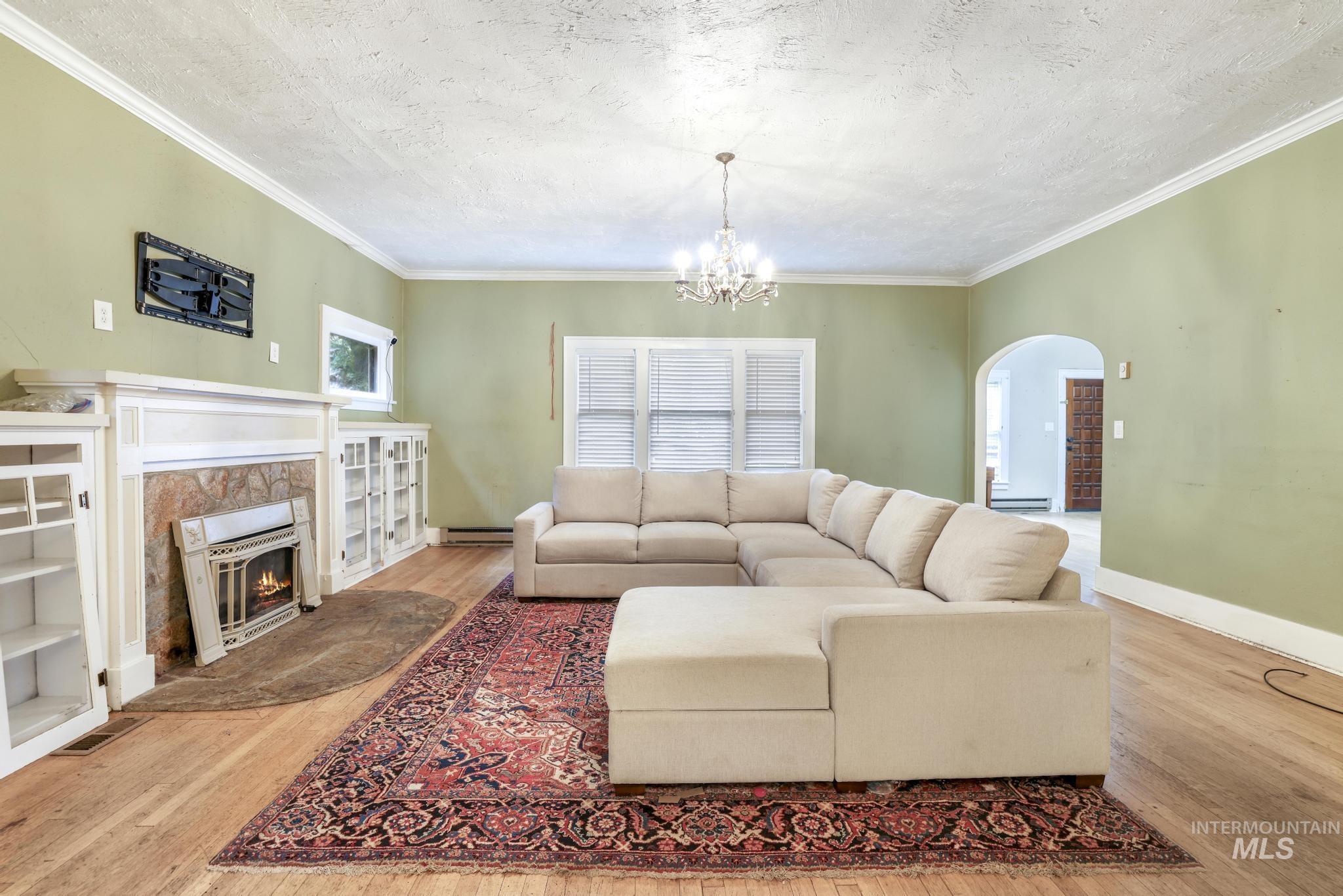 Living area featuring arched walkways, a chandelier, a textured ceiling, ornamental molding, and a high end fireplace