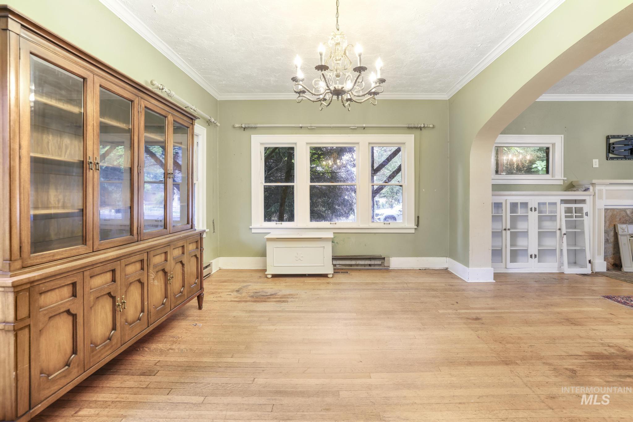 Unfurnished dining area featuring light wood-type flooring, ornamental molding, arched walkways, a chandelier, and baseboard heating