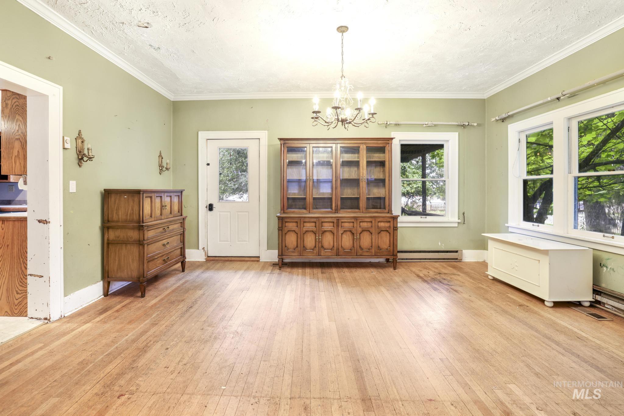Dining room featuring light wood-style floors, a chandelier, a textured ceiling, crown molding, and a baseboard heating unit