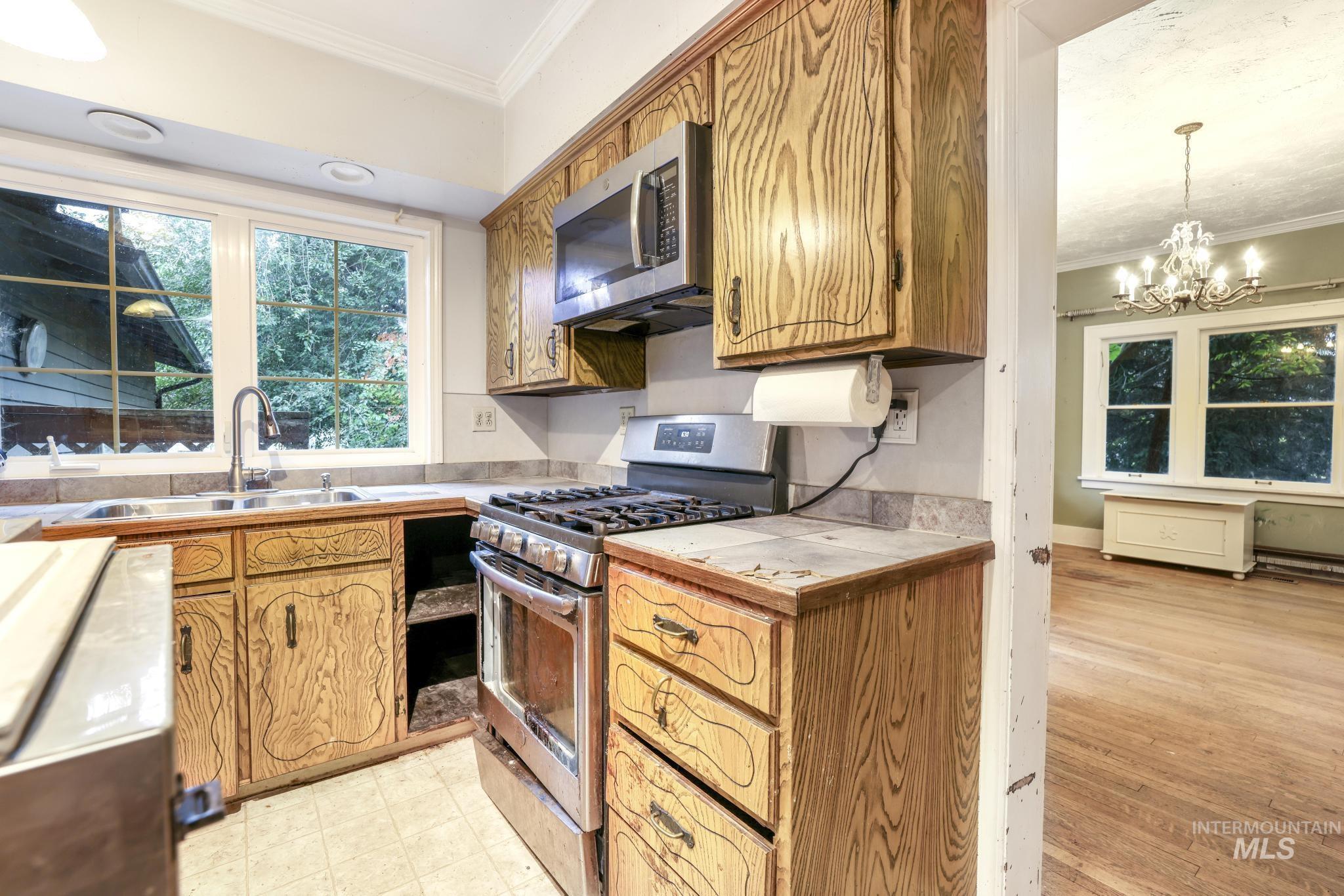 Kitchen with ornamental molding, appliances with stainless steel finishes, healthy amount of natural light, brown cabinets, and a chandelier
