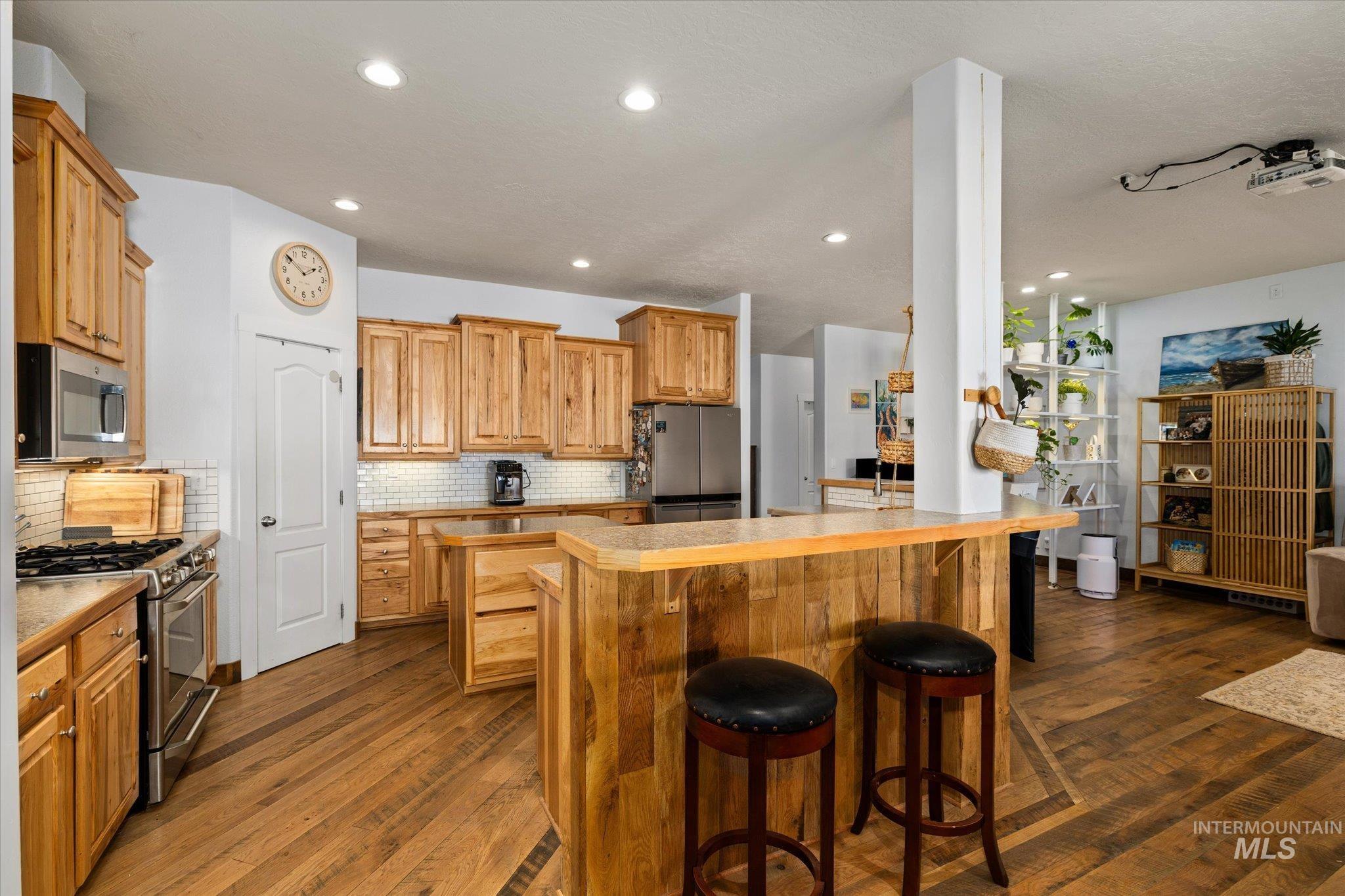 Kitchen with a kitchen bar, appliances with stainless steel finishes, dark wood-type flooring, recessed lighting, and tasteful backsplash