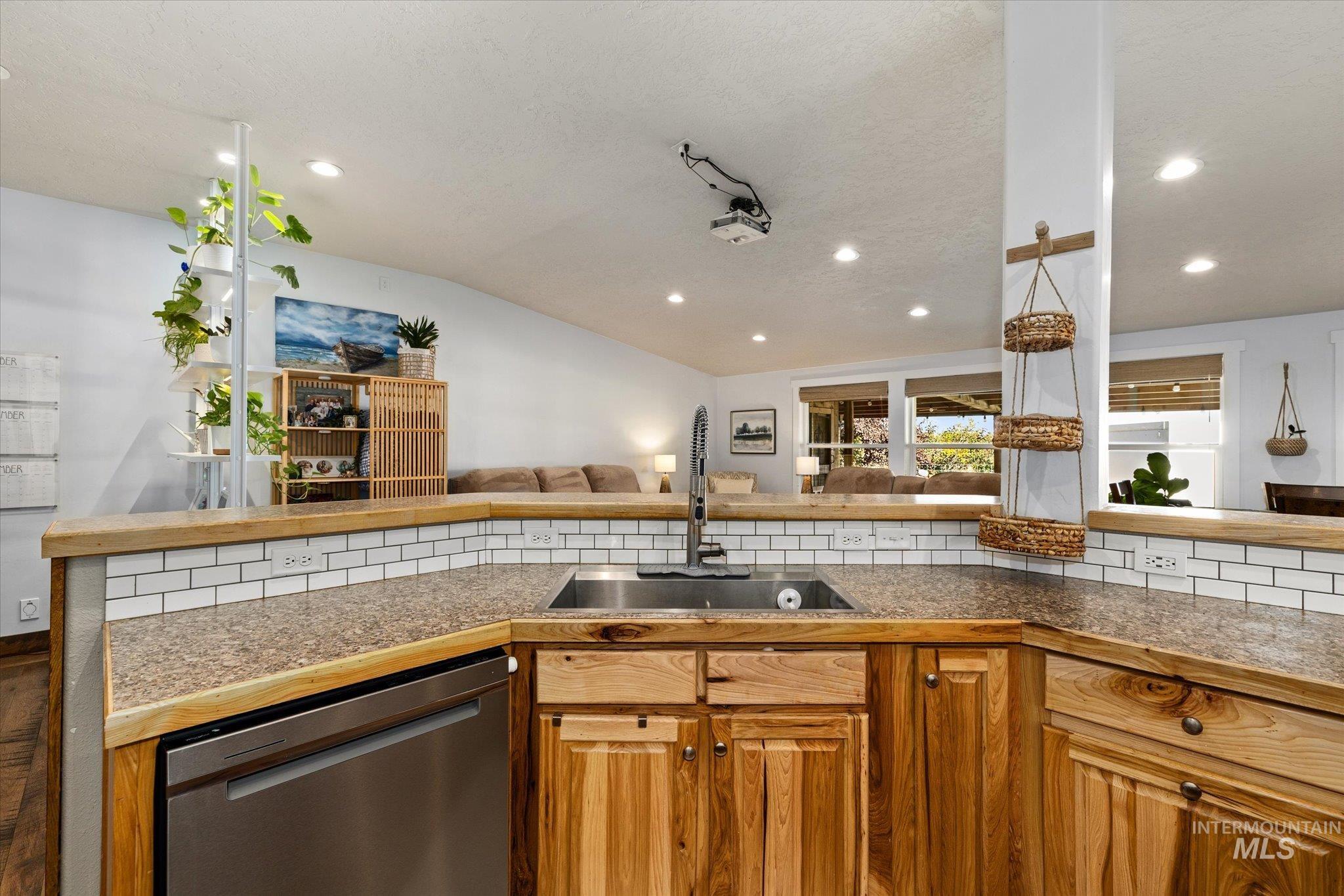 Kitchen with brown cabinets, stainless steel dishwasher, open floor plan, recessed lighting, and tile counters