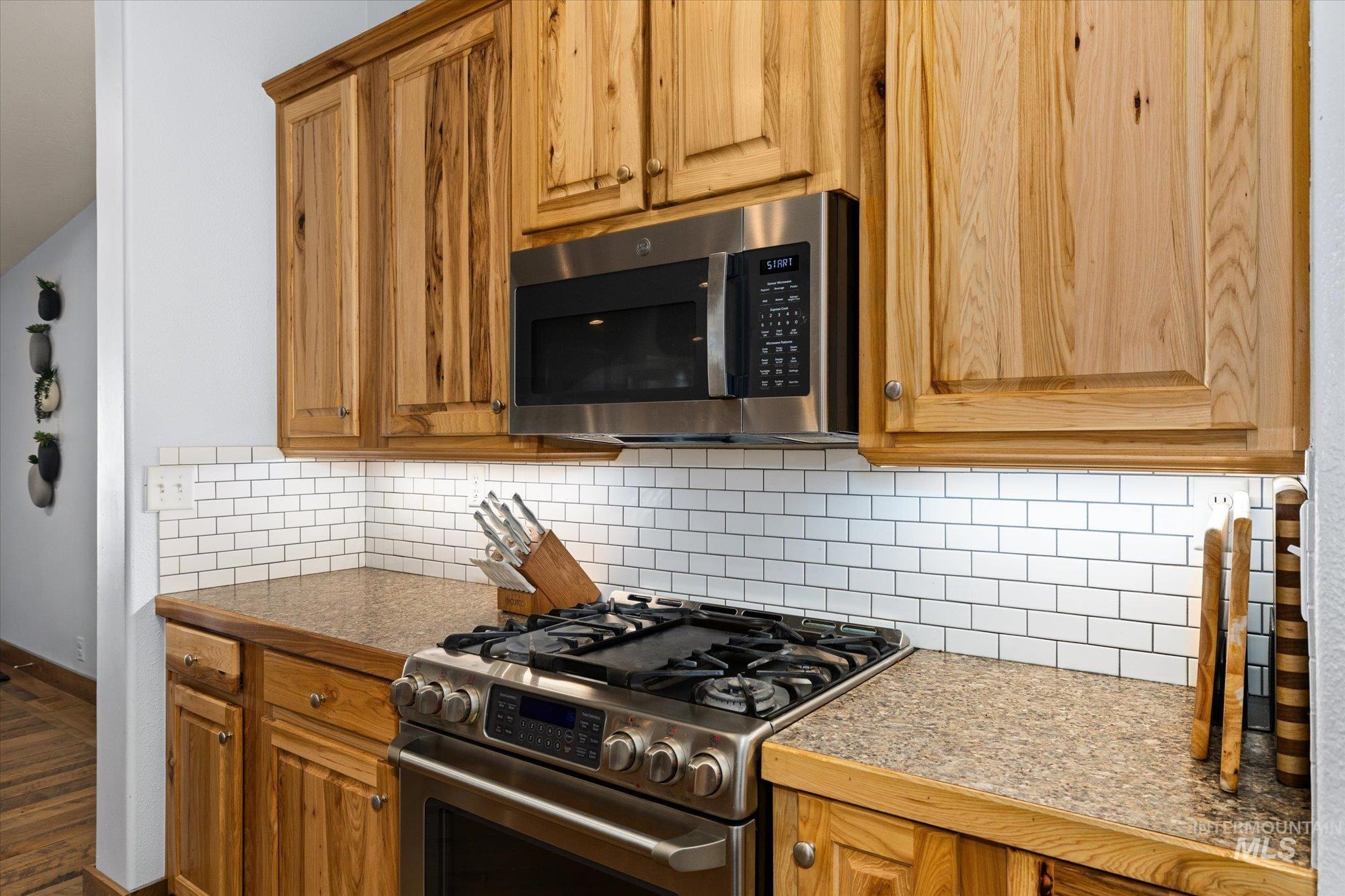 Kitchen featuring stainless steel appliances, tasteful backsplash, dark wood-style flooring, and brown cabinets