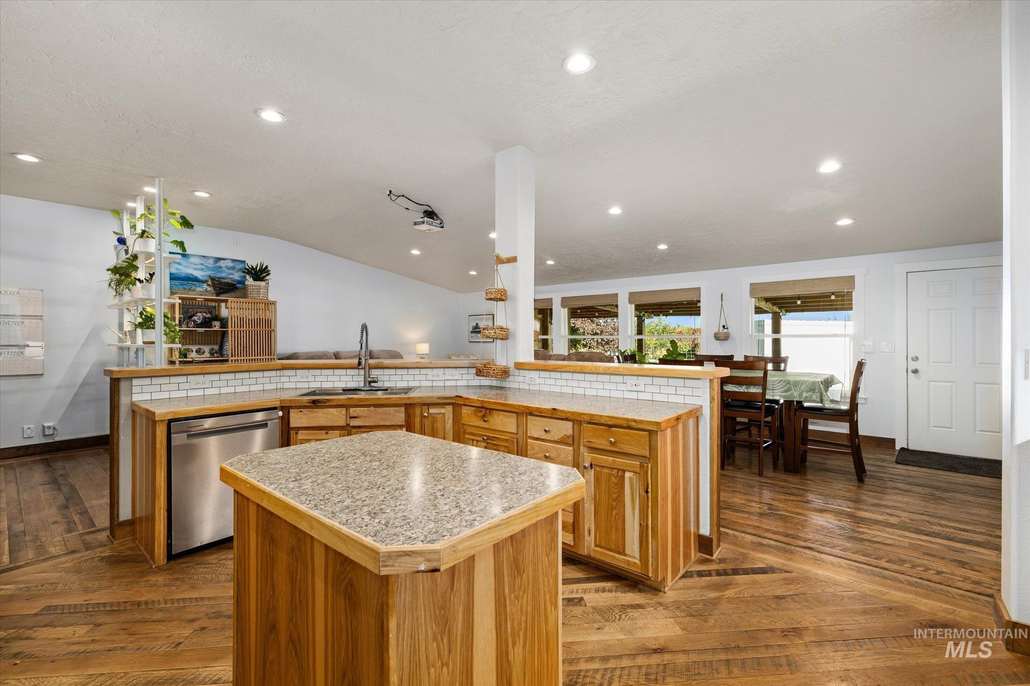 Kitchen featuring light countertops, a kitchen island, dark wood-type flooring, recessed lighting, and stainless steel dishwasher