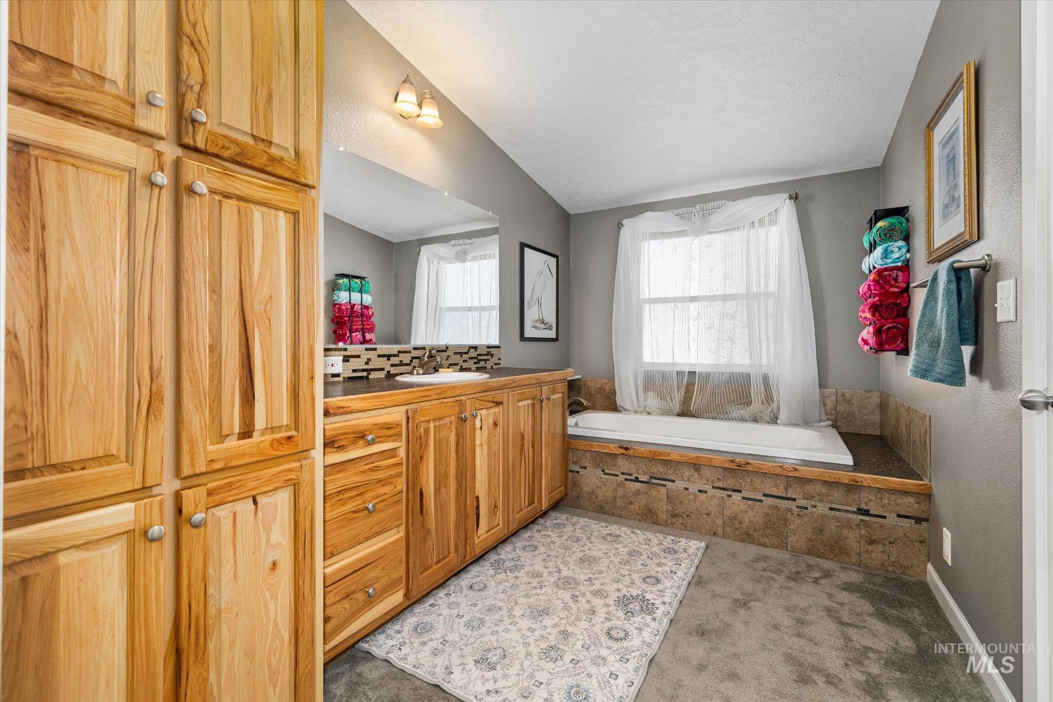 Bathroom featuring a garden tub, vanity, lofted ceiling, backsplash, and light carpet