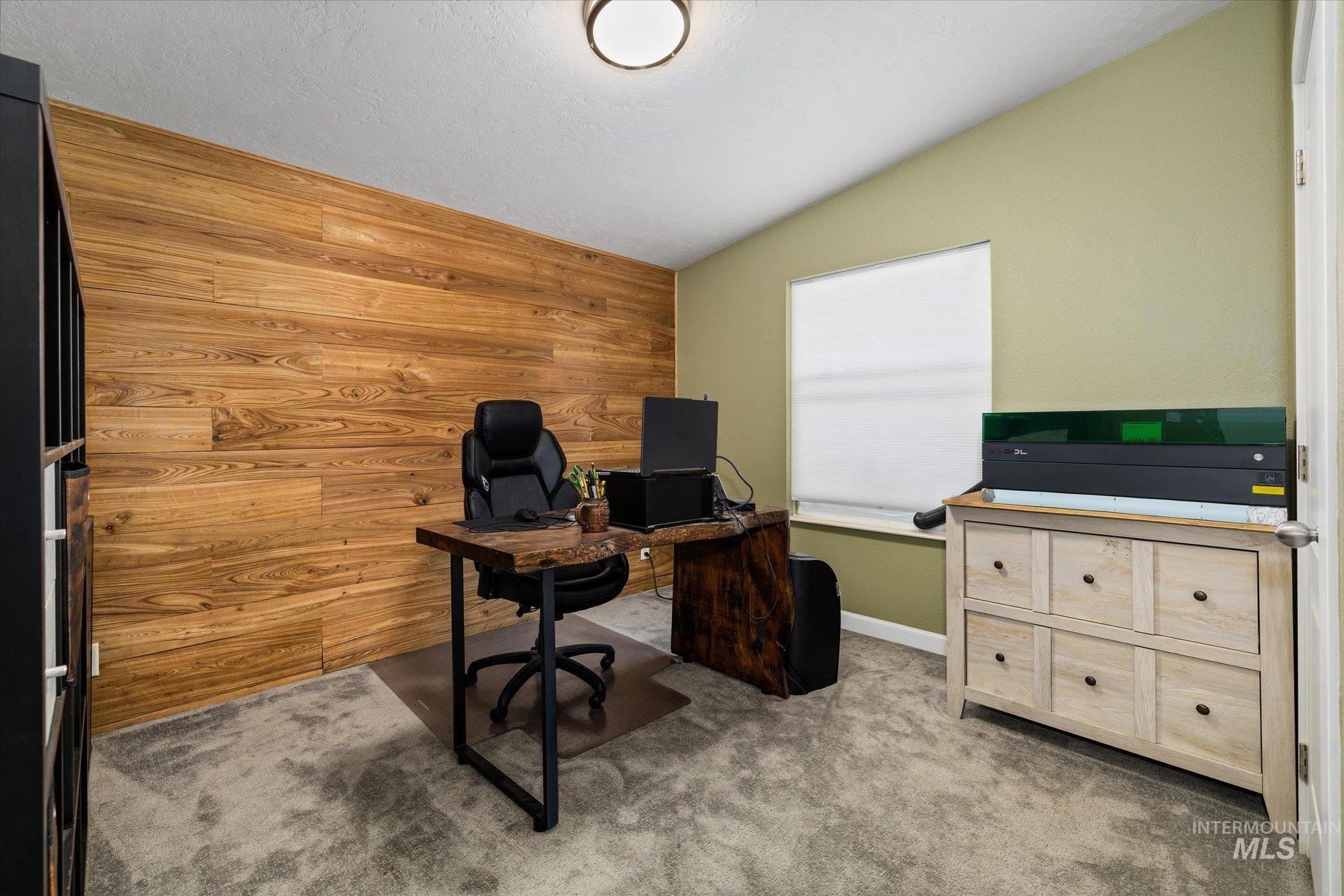 Home office featuring wood walls, light colored carpet, vaulted ceiling, and a textured ceiling