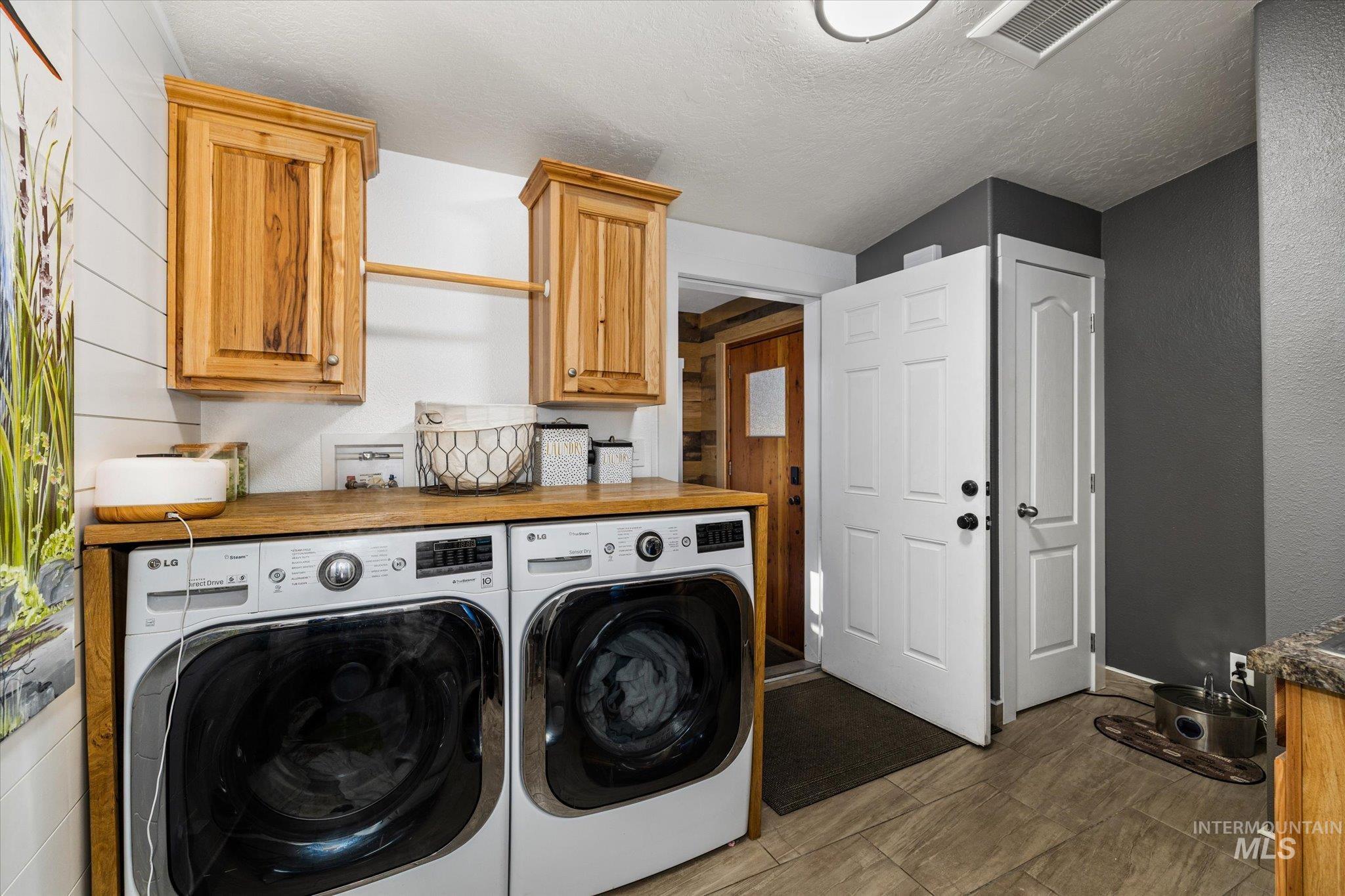 Laundry area with a textured ceiling, independent washer and dryer, wood walls, and cabinet space