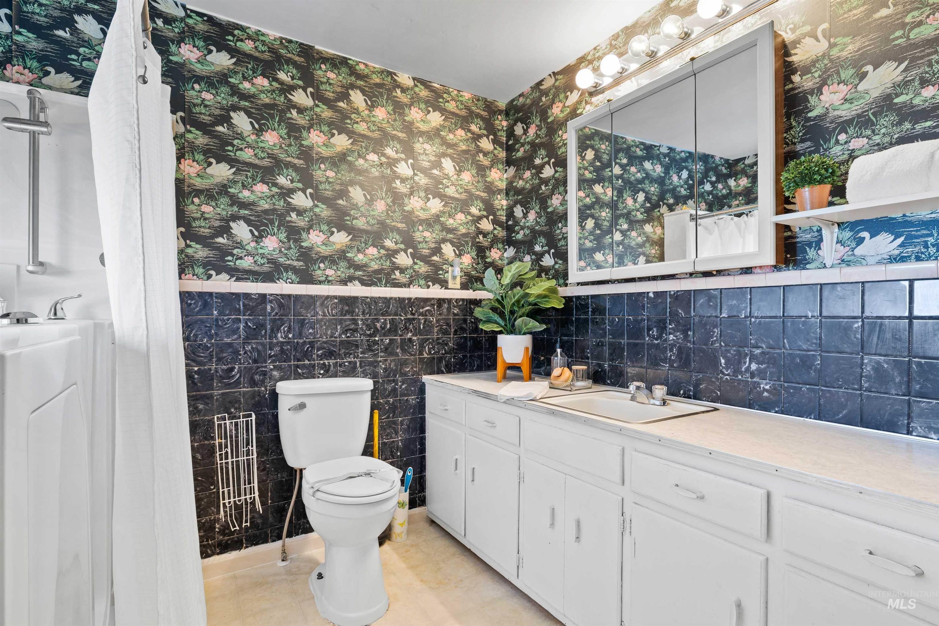 Bathroom with wallpapered walls, tile walls, a wainscoted wall, vanity, and light tile patterned floors