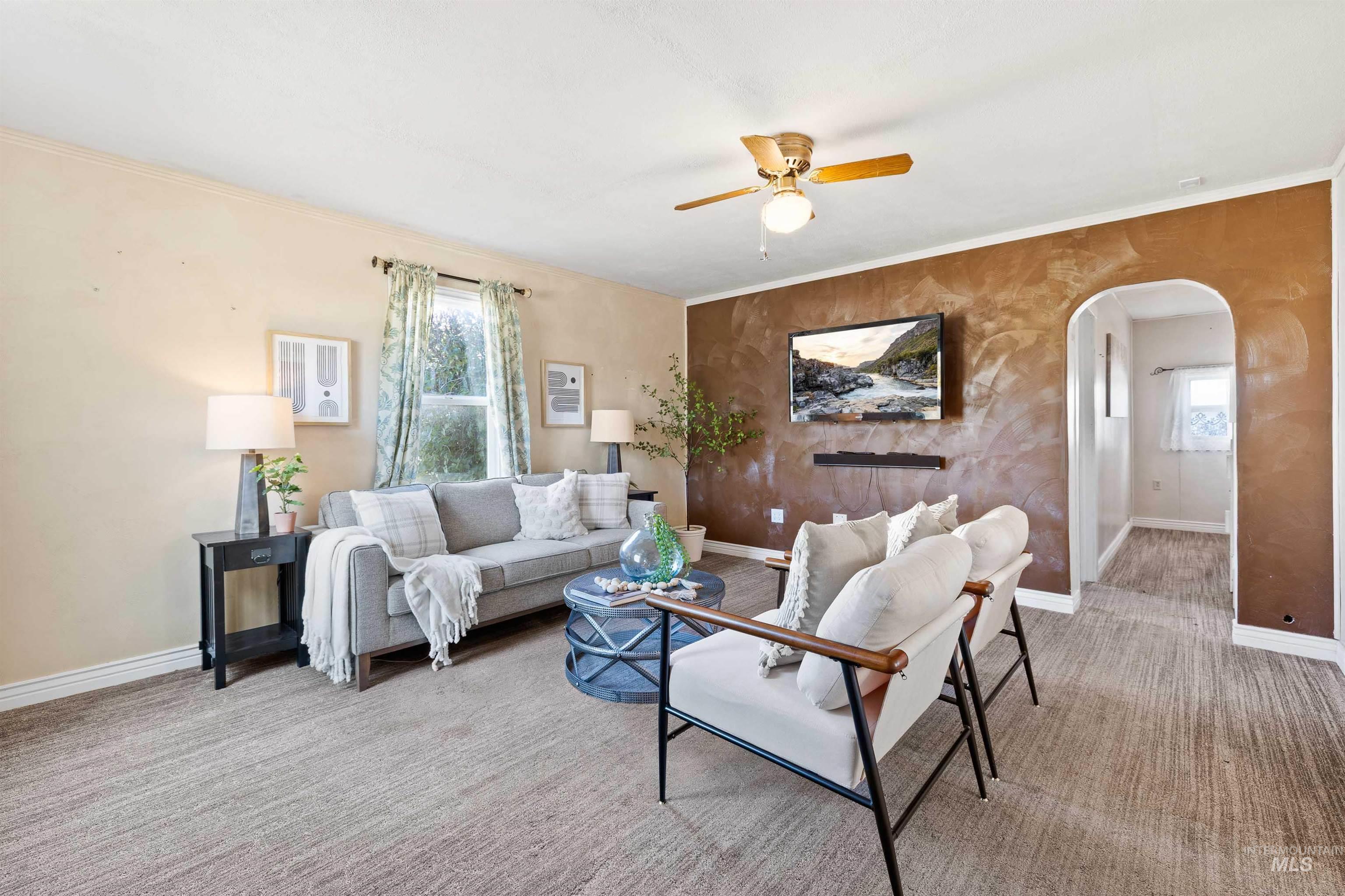 Carpeted living area with arched walkways, ornamental molding, and a ceiling fan