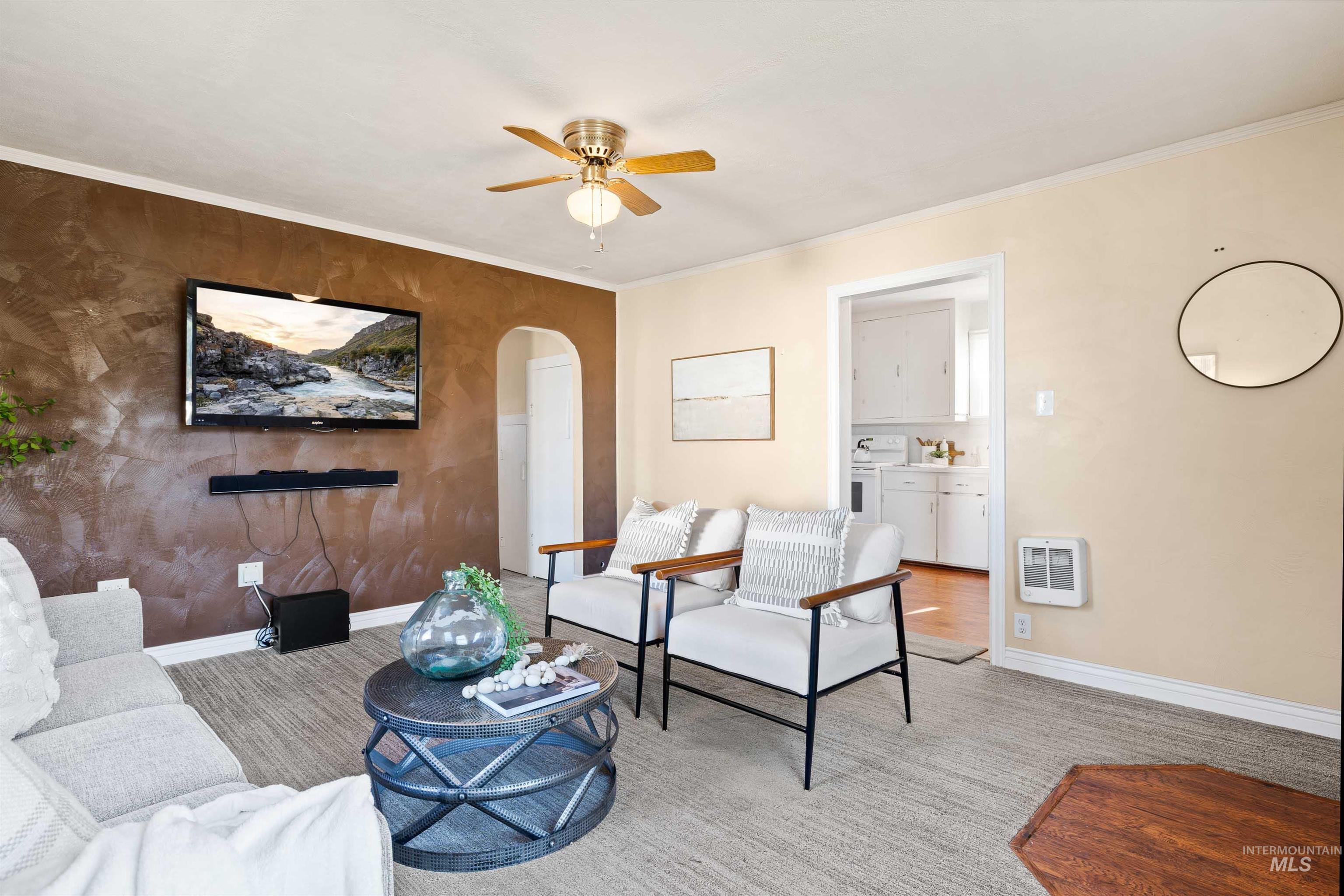 Living area featuring crown molding, arched walkways, ceiling fan, heating unit, and carpet floors