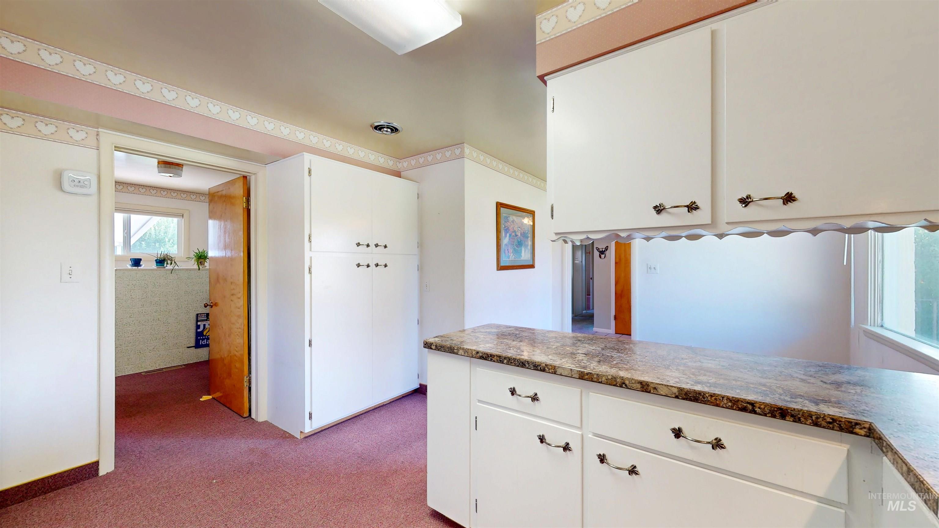 Kitchen featuring dark colored carpet and white cabinets