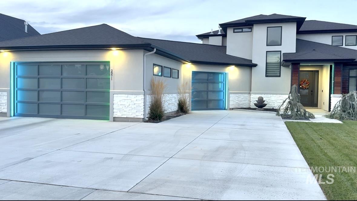 View of front of property with stone siding, a garage, driveway, and stucco siding