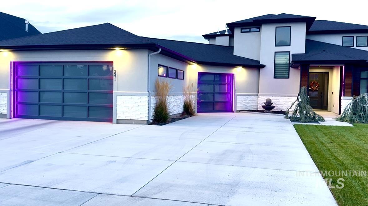 View of front facade with stone siding, a garage, driveway, and stucco siding