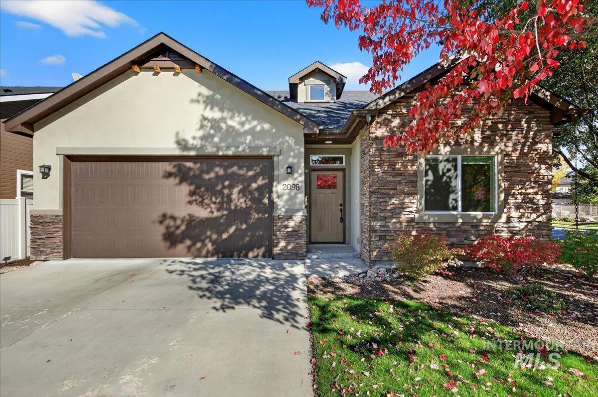 View of front of house with stone siding, driveway, an attached garage, and stucco siding