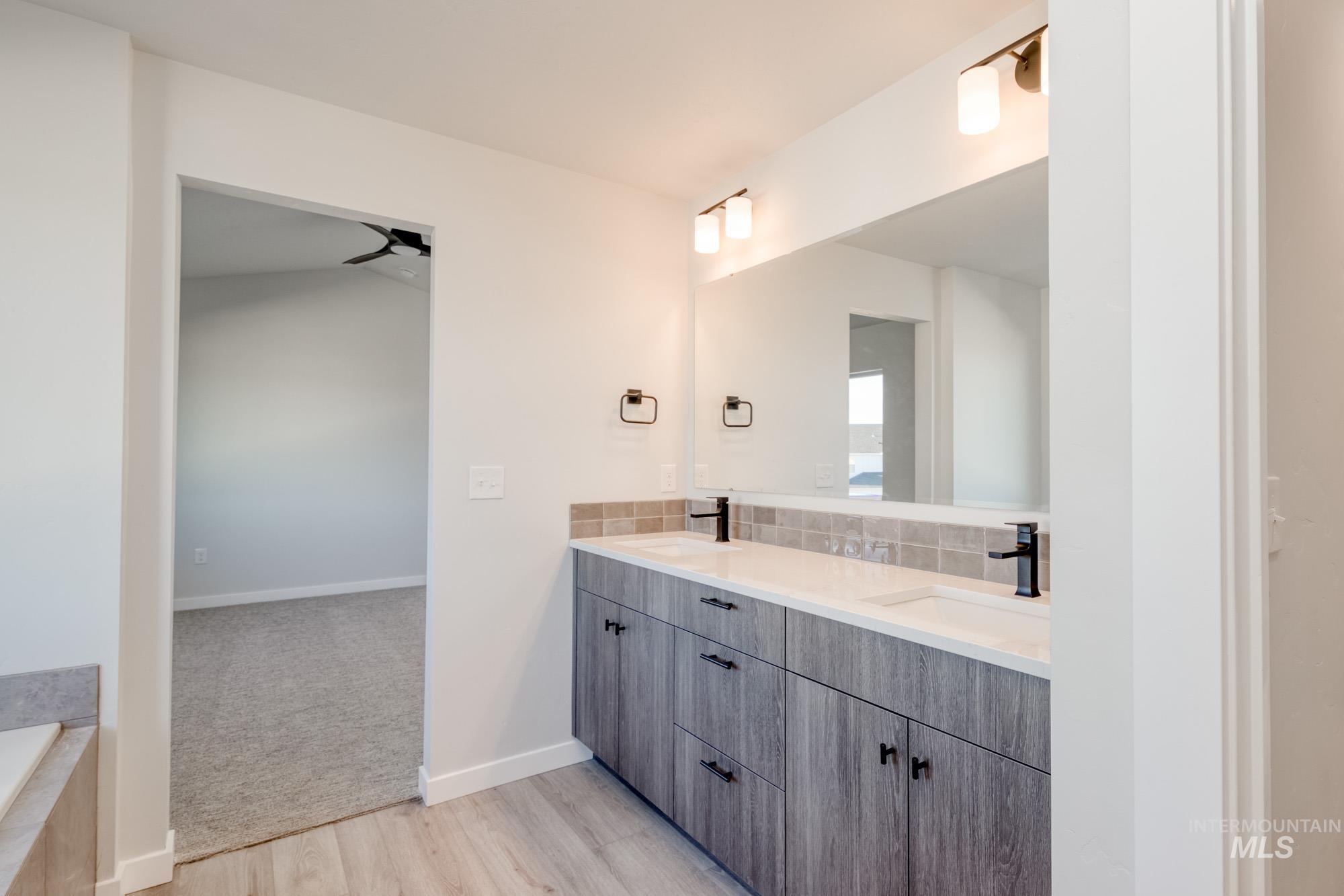 Bathroom with double vanity, light wood finished floors, backsplash, and a bathtub