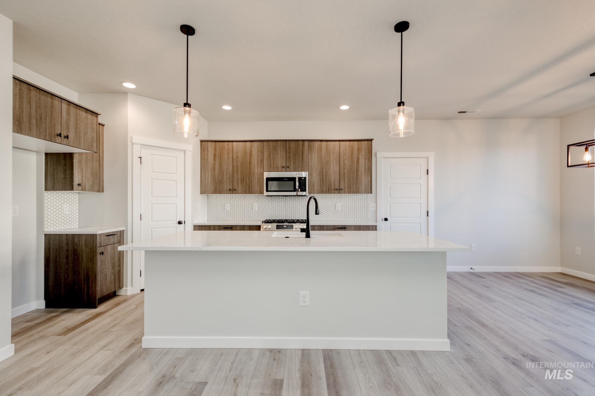 Kitchen featuring brown cabinetry, decorative backsplash, an island with sink, pendant lighting, and light wood finished floors