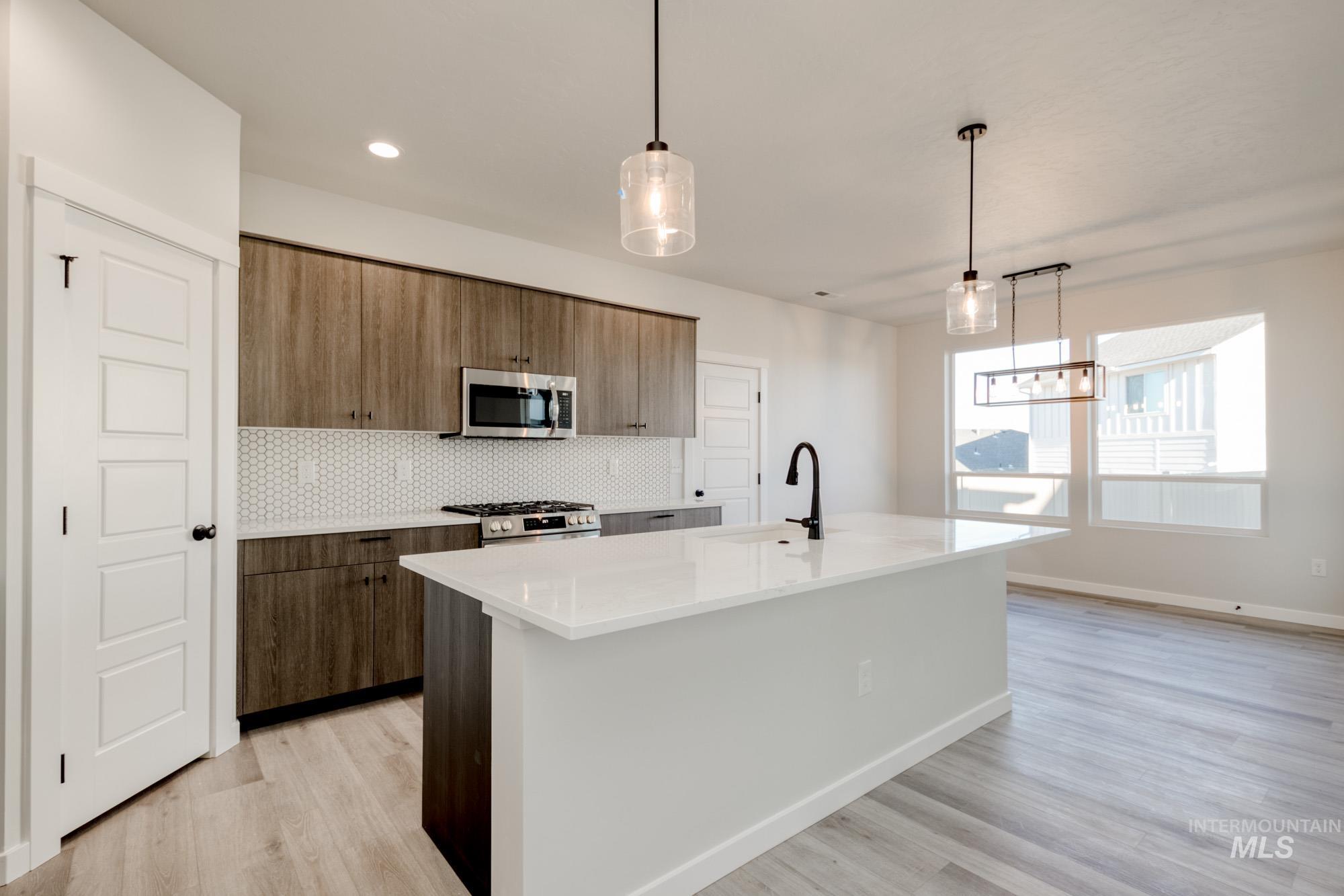 Kitchen featuring tasteful backsplash, decorative light fixtures, light stone countertops, a center island with sink, and stainless steel appliances