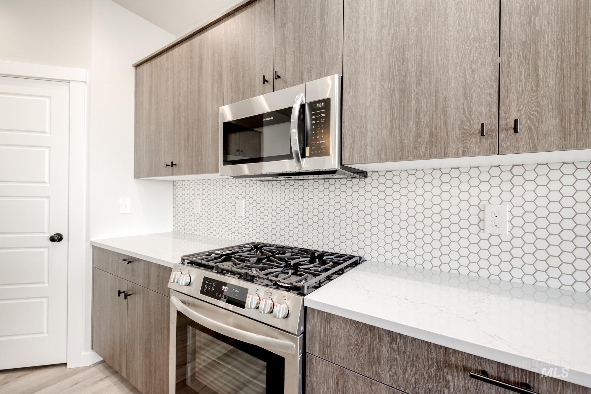 Kitchen with stainless steel appliances, light stone counters, decorative backsplash, and light brown cabinetry