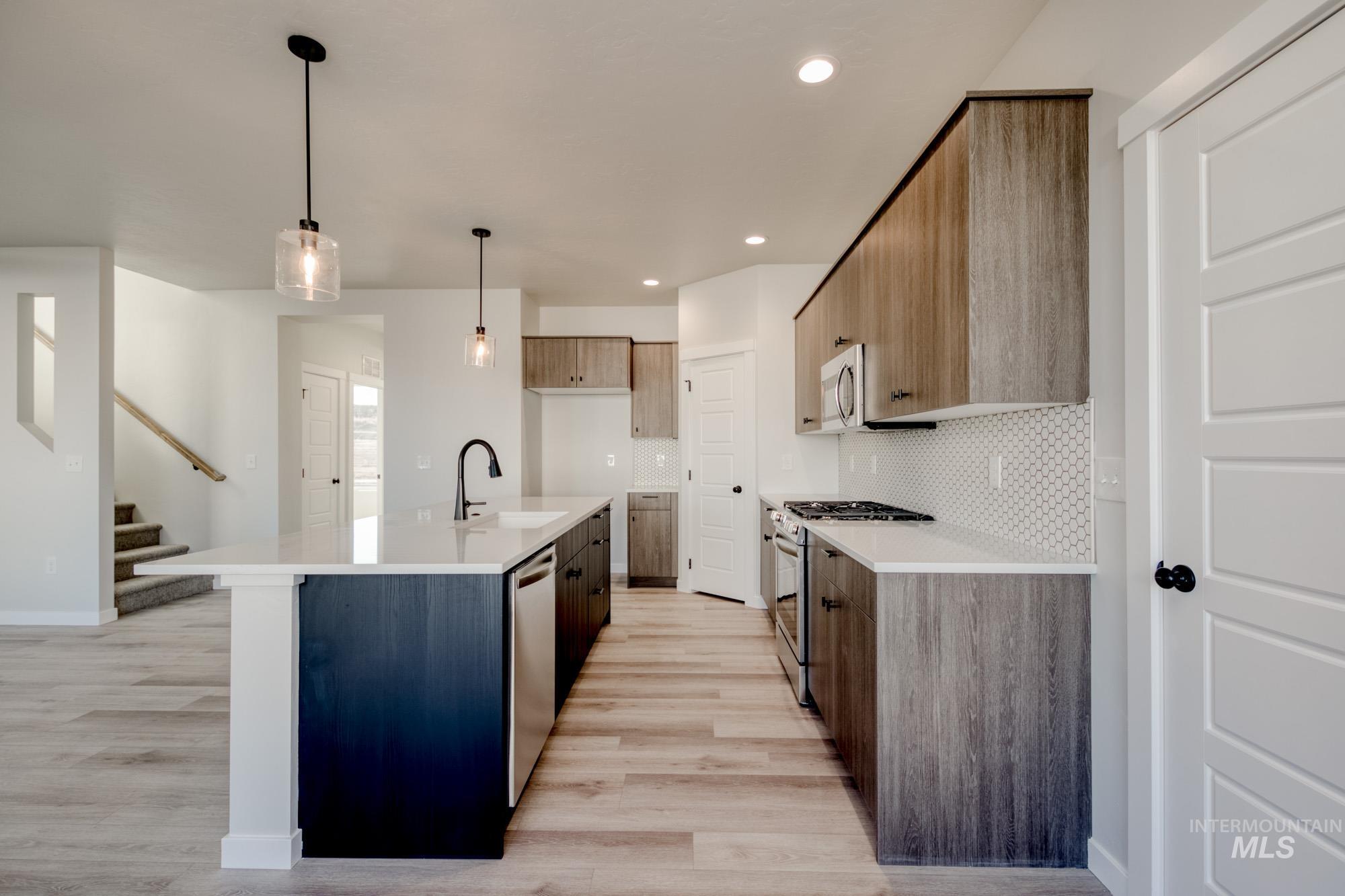 Kitchen featuring appliances with stainless steel finishes, tasteful backsplash, hanging light fixtures, a kitchen island with sink, and recessed lighting