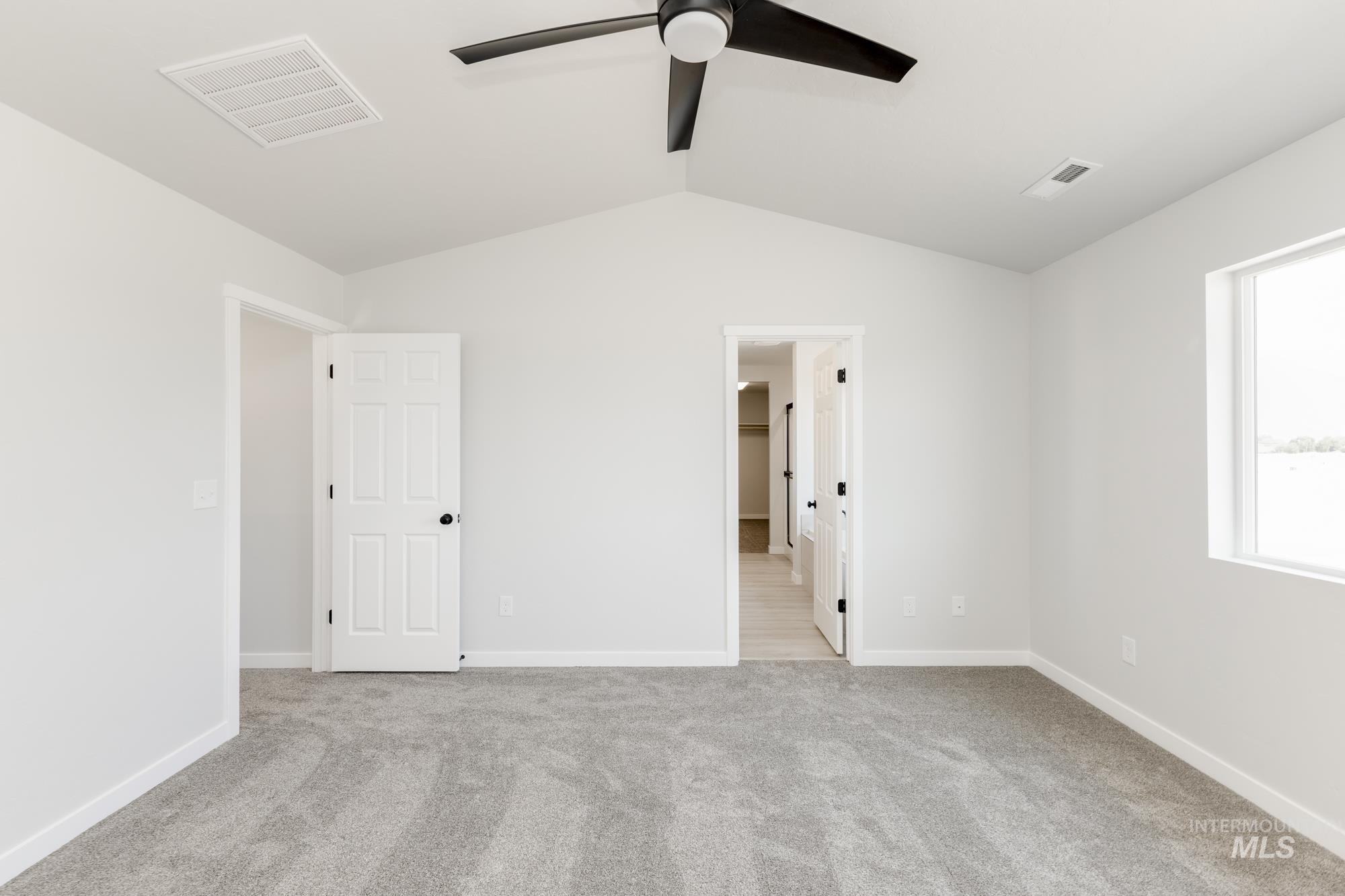 Unfurnished bedroom with vaulted ceiling, light carpet, ensuite bathroom, and ceiling fan