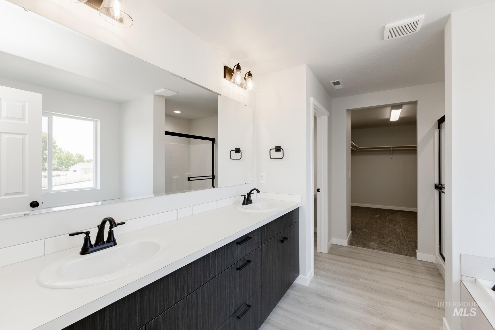 Full bath featuring double vanity, a shower stall, a spacious closet, and light wood-type flooring