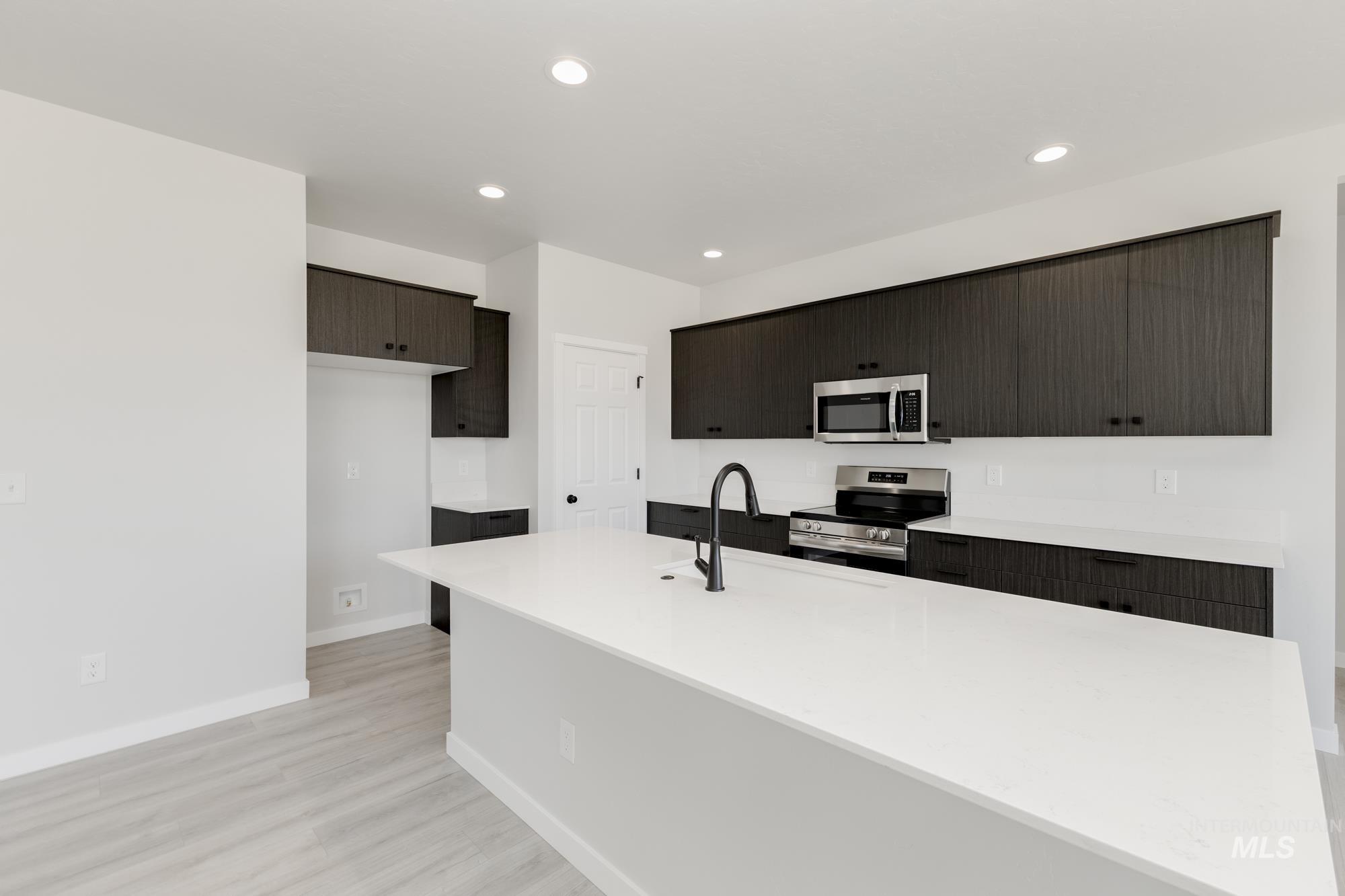 Kitchen with appliances with stainless steel finishes, a kitchen island with sink, light wood-style flooring, light stone countertops, and recessed lighting