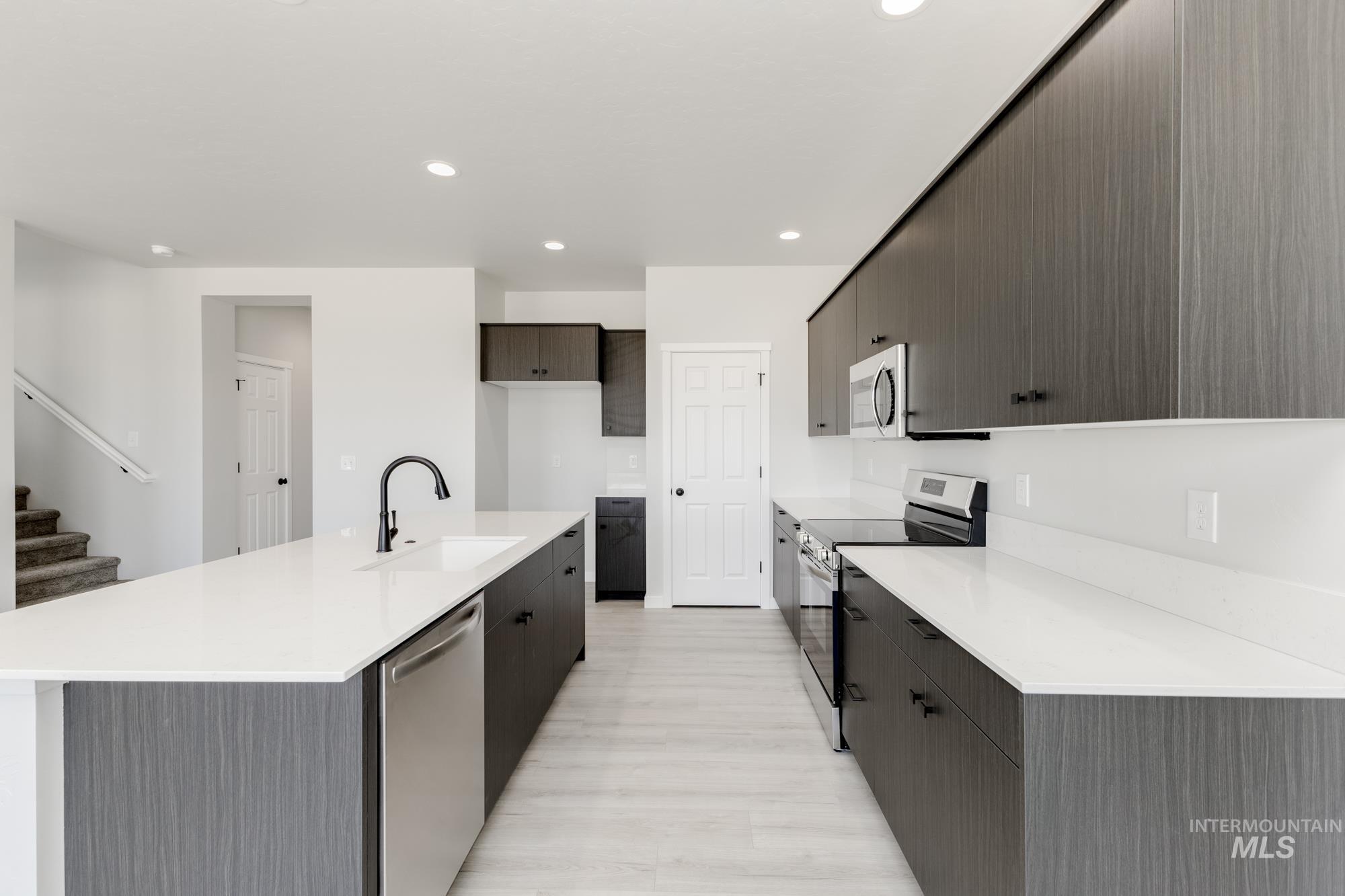 Kitchen featuring stainless steel appliances, modern cabinets, recessed lighting, light stone countertops, and a center island with sink