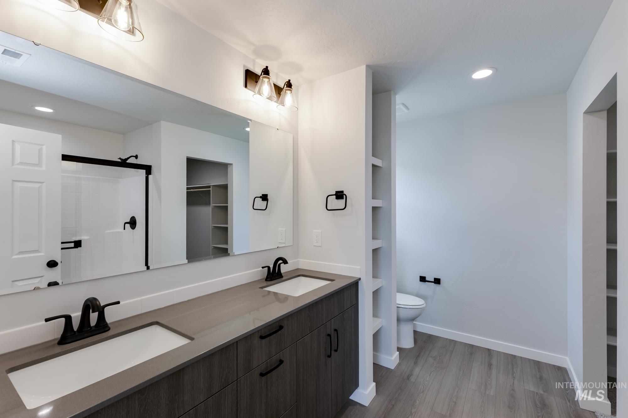 Full bath with a spacious closet, recessed lighting, light wood-type flooring, double vanity, and a shower stall